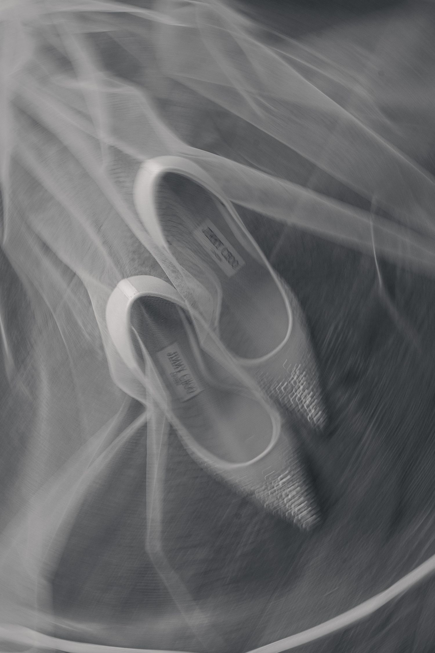 Black and white photo of elegant bridal heels resting on a flowing wedding veil.