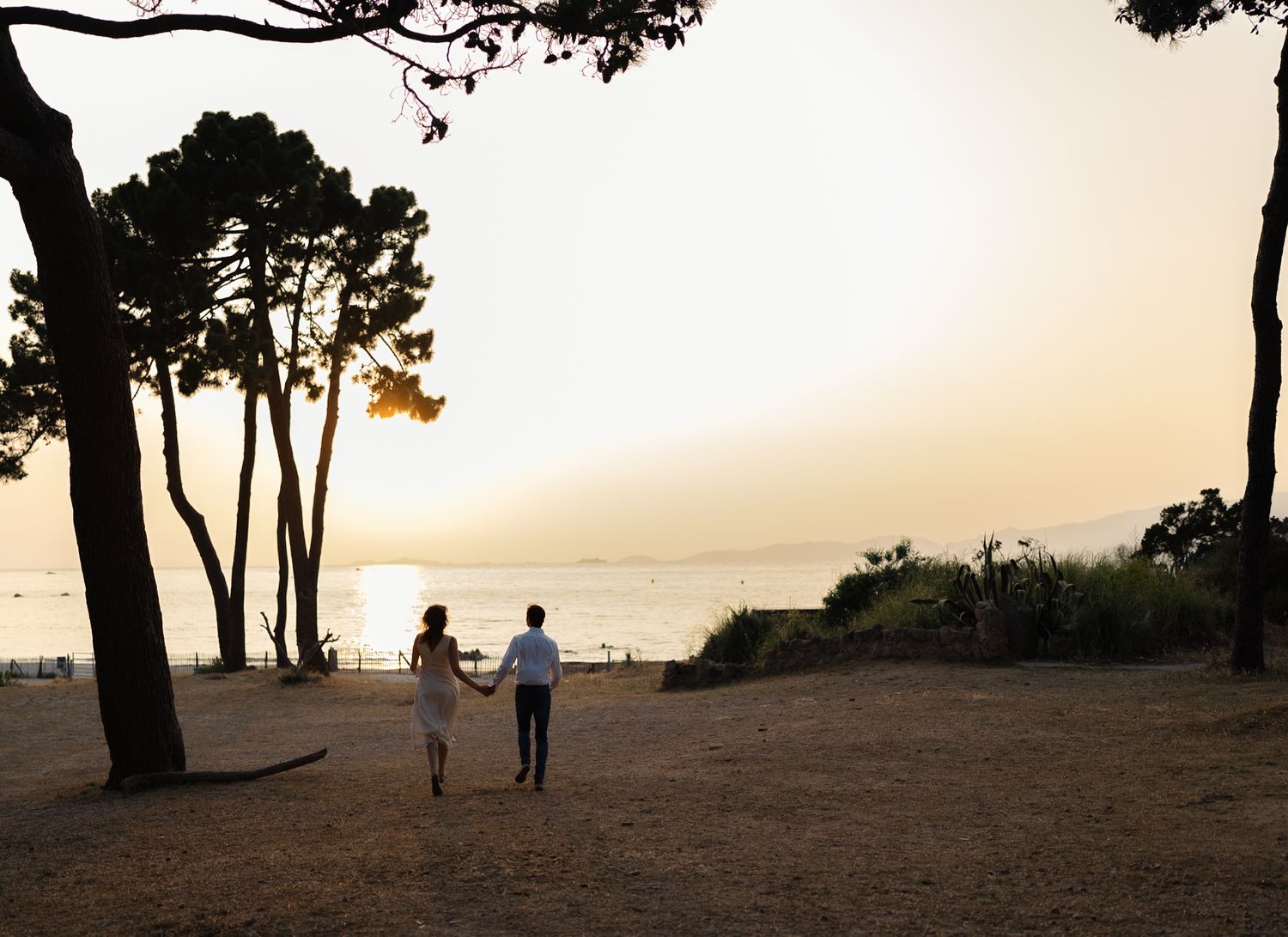 Silhouettes of people walking on a coastal path during sunset with trees in the background.