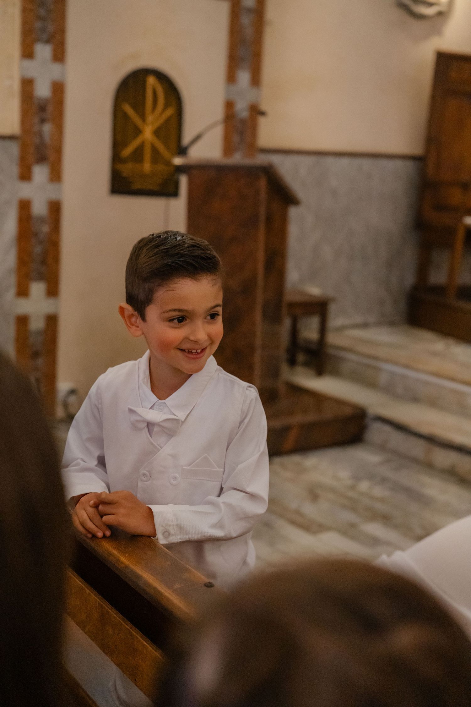 Young children in white dress shirts sit attentively in wooden church pews during a religious service.