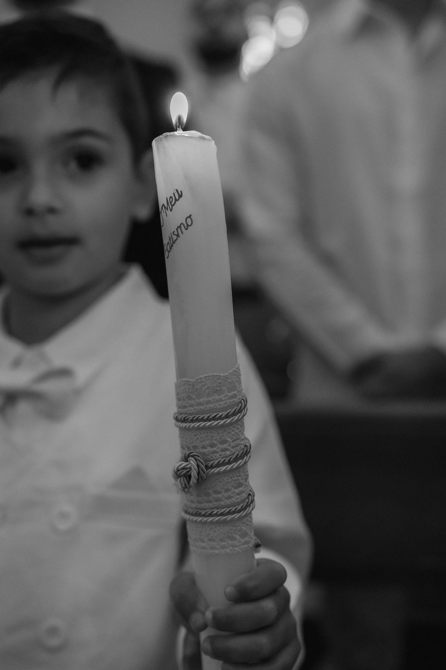 A lit white ceremonial candle with decorative rope wrapping being held in black and white.