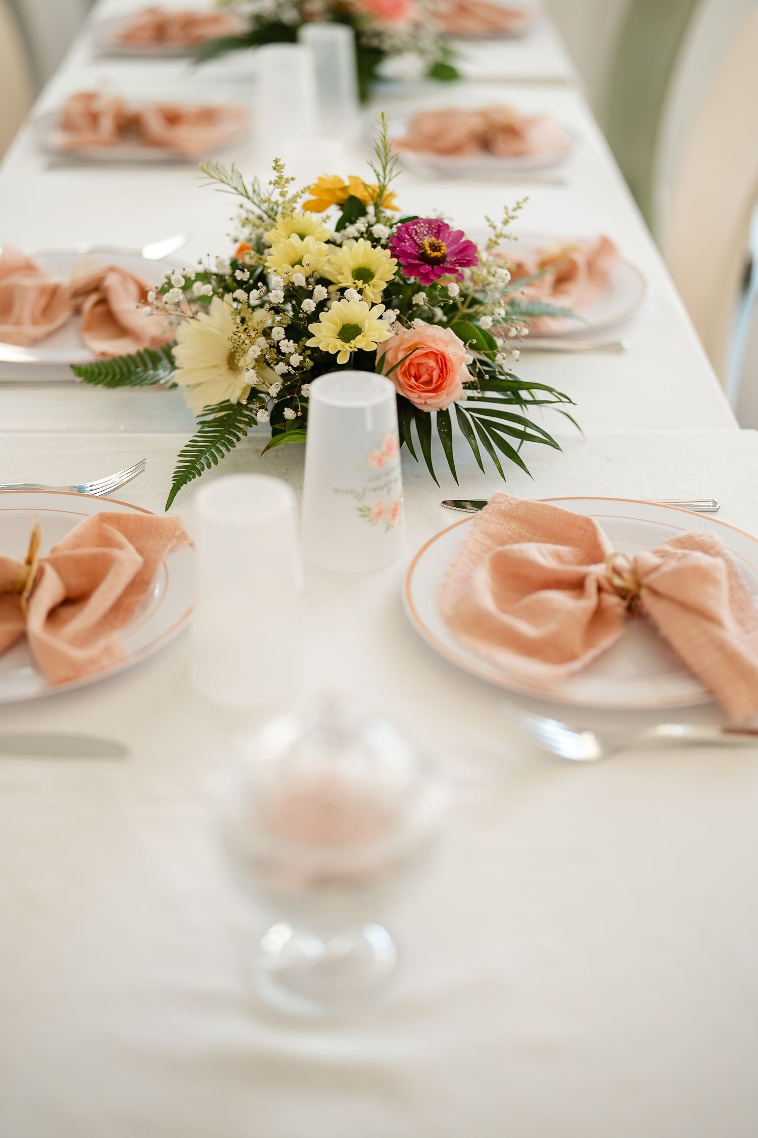 Elegant wedding table settings with peach napkins and fresh floral centerpieces in white and coral tones.