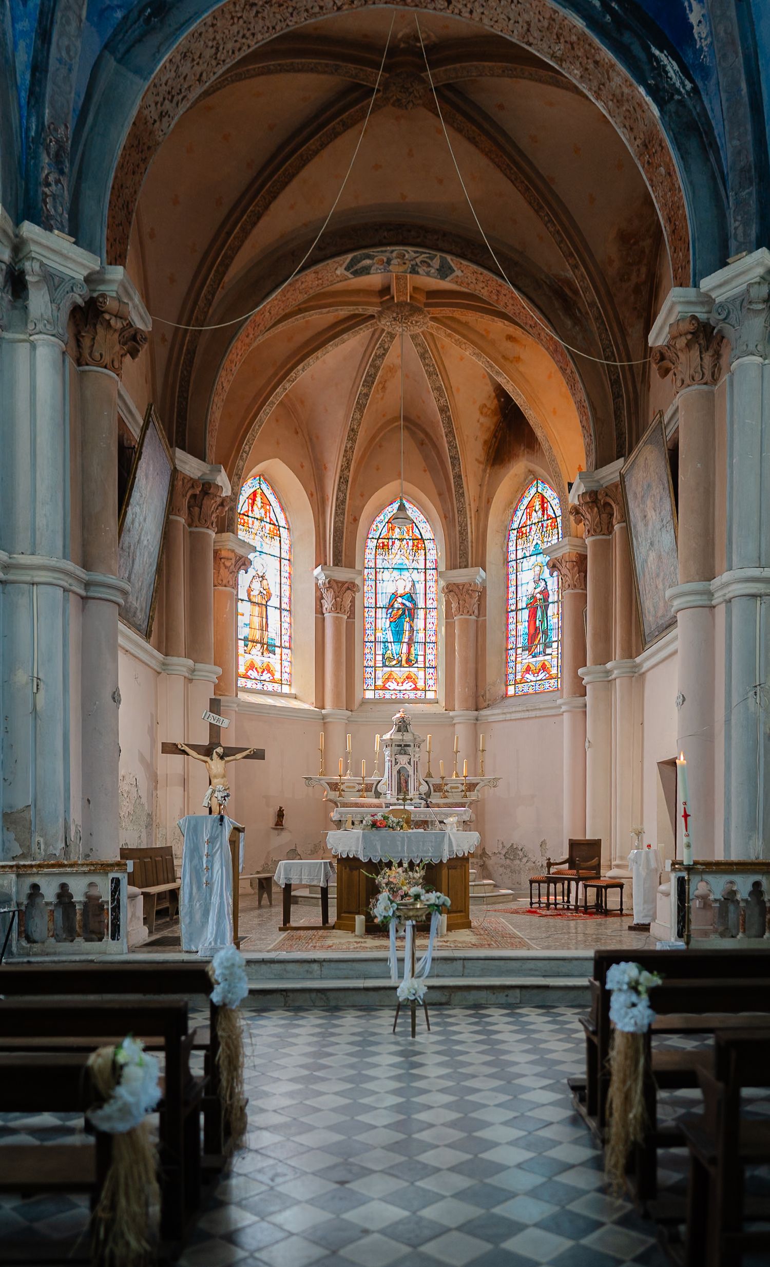 Panoramic view of a traditional church interior with stained glass windows, vaulted ceilings, and checkered floor.
