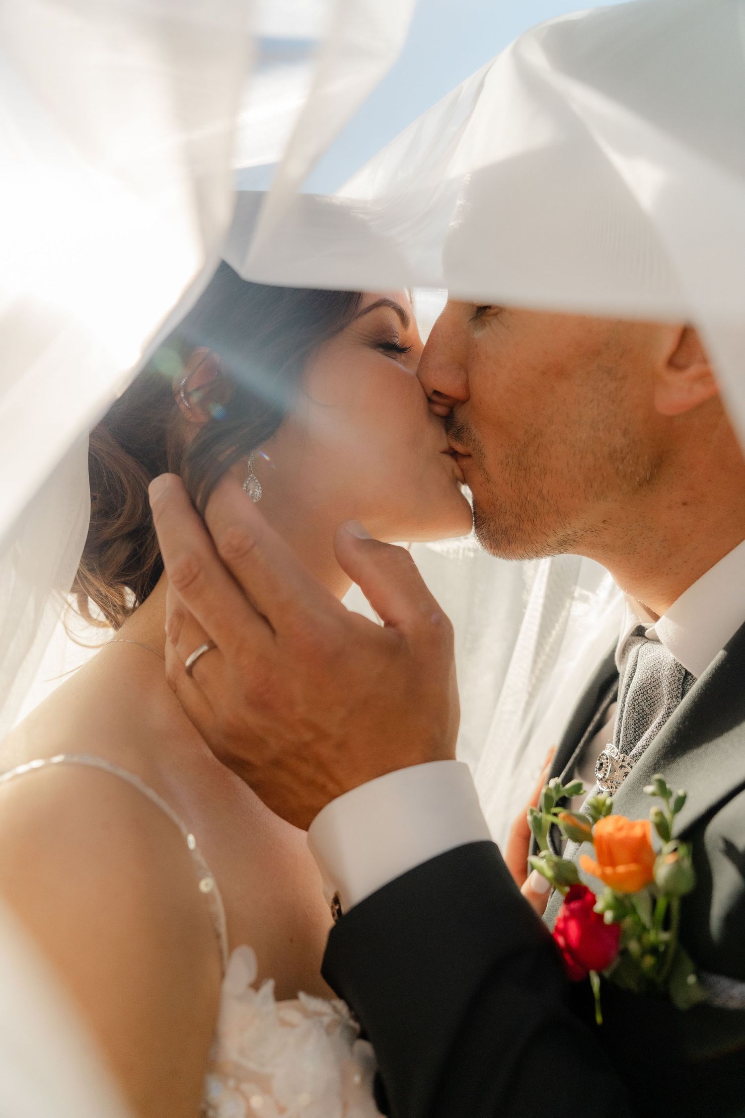 Bride and groom sharing a romantic kiss under a flowing white veil on their wedding day.