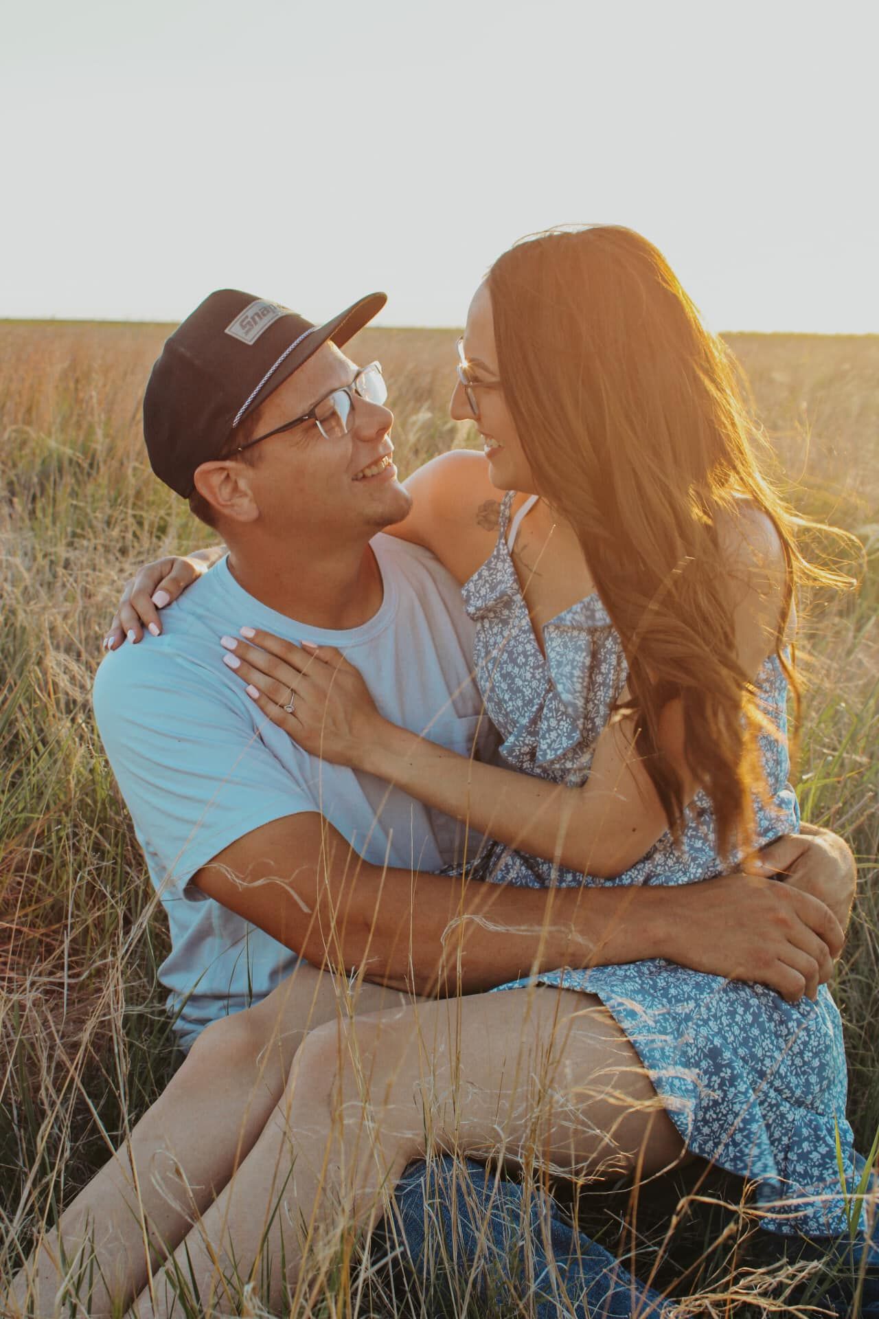 A couple shares a tender moment while sitting in tall grass during golden hour.