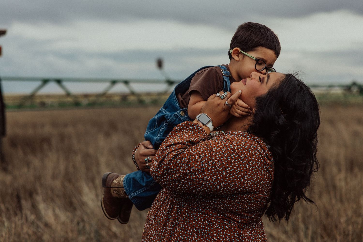 A romantic couple embraces tenderly in a golden field during sunset while wearing coordinated earth-toned outfits.