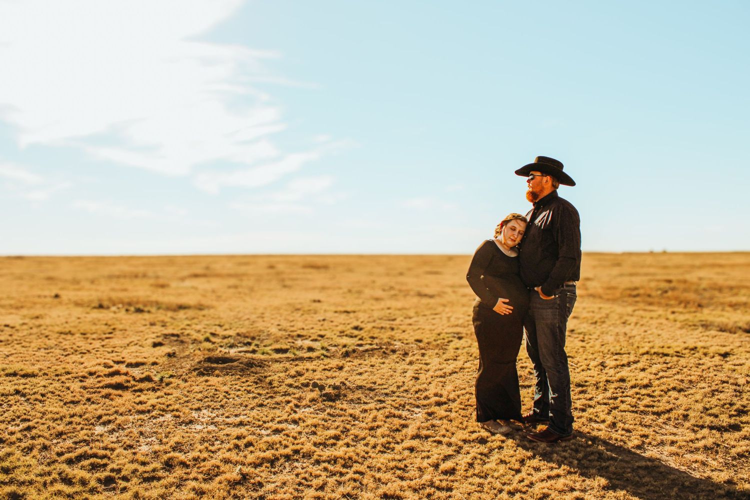Two people embrace while standing in a vast, barren desert landscape under bright blue sky.