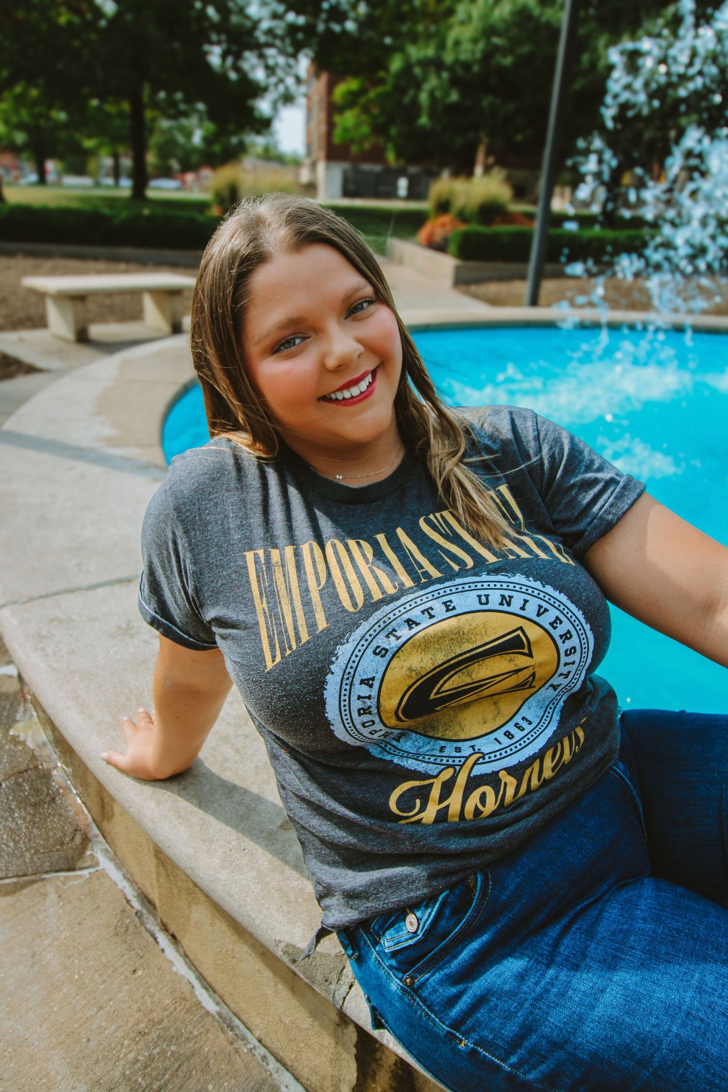 A person wearing a gray t-shirt sits by a swimming pool on a sunny day.