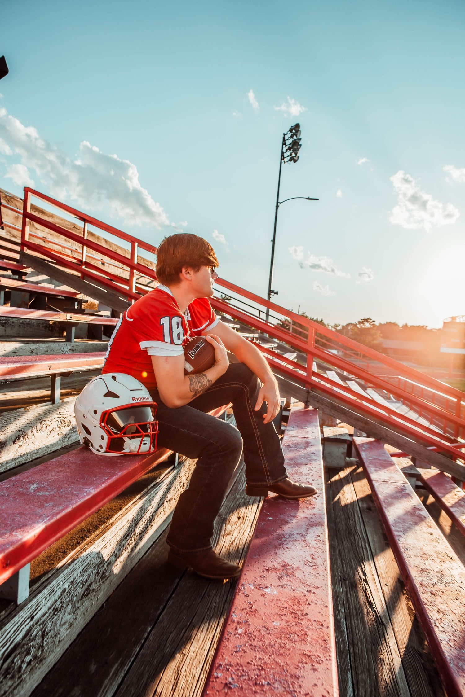 A football player sits alone on stadium bleachers at sunset wearing a red jersey number 10.