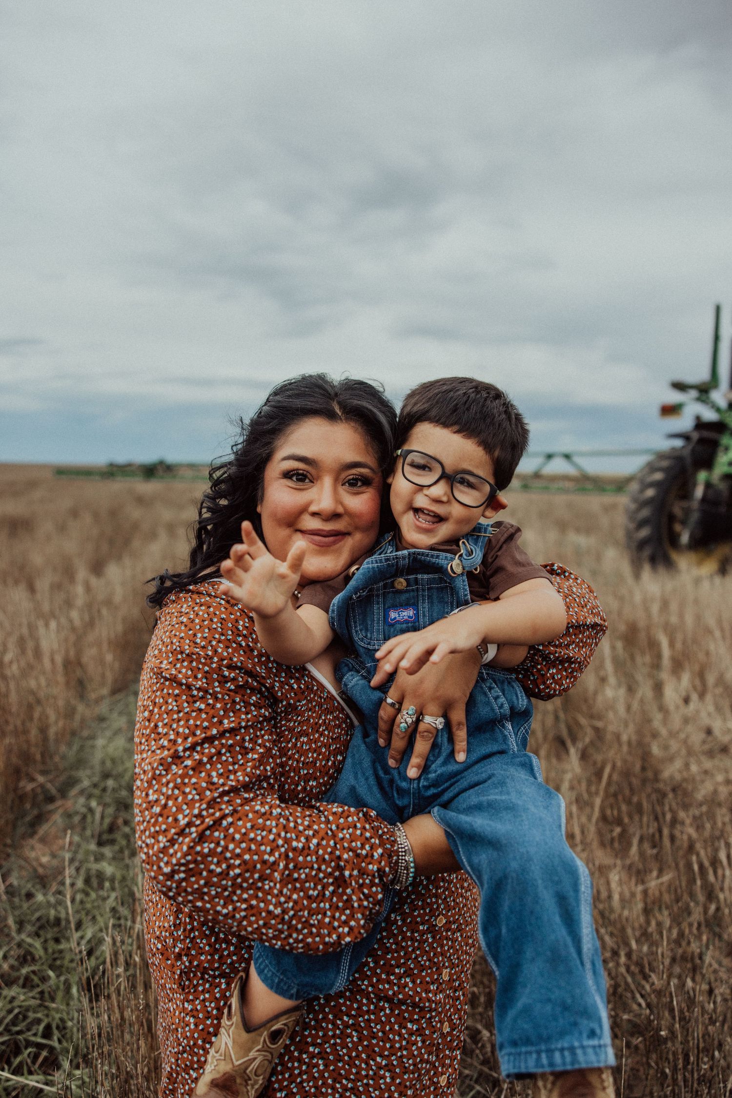 A mother and child share joyful embraces in a golden field on an overcast day.