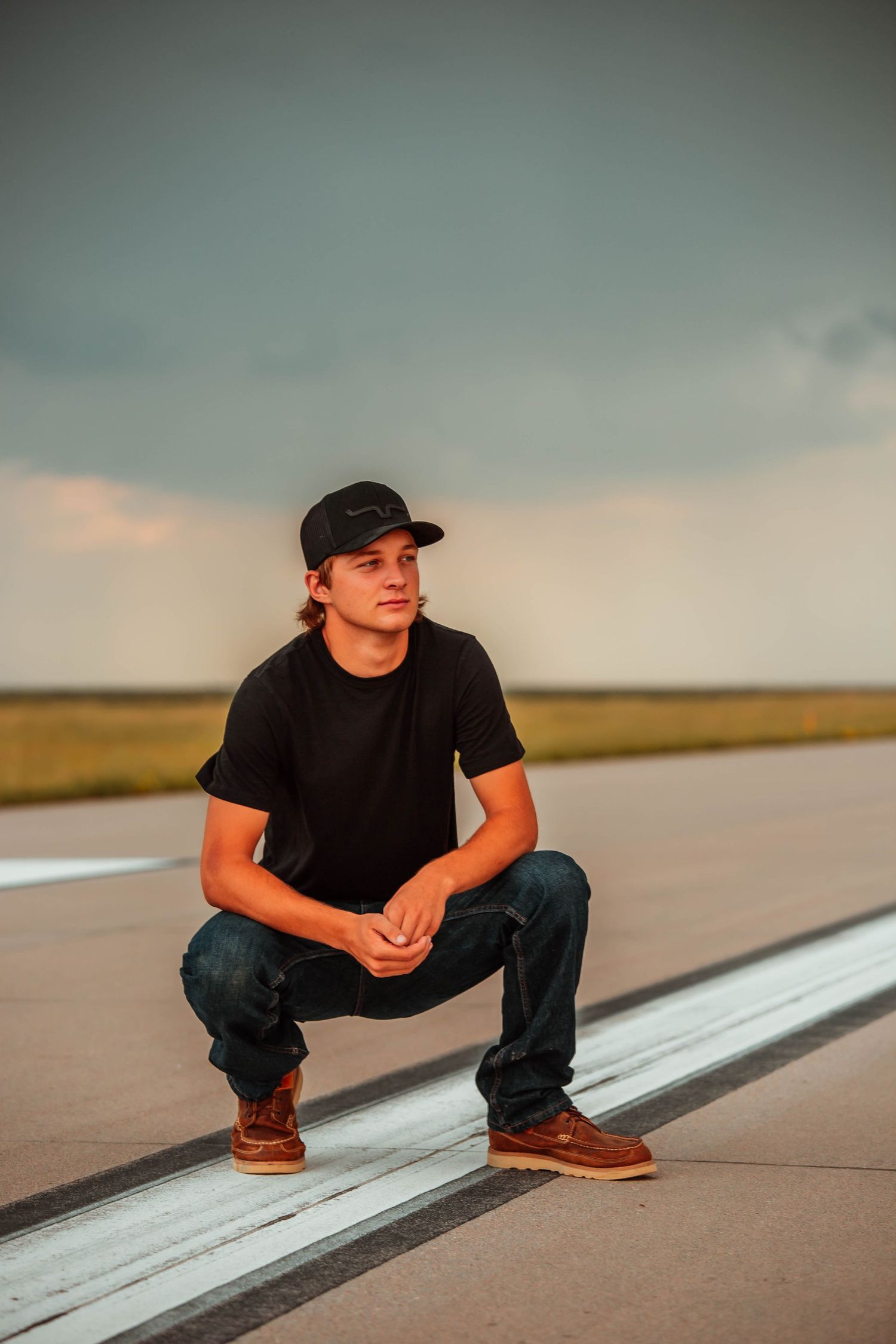 A person in black clothing and baseball cap crouches on a white line in a sequence of similar poses at sunset.