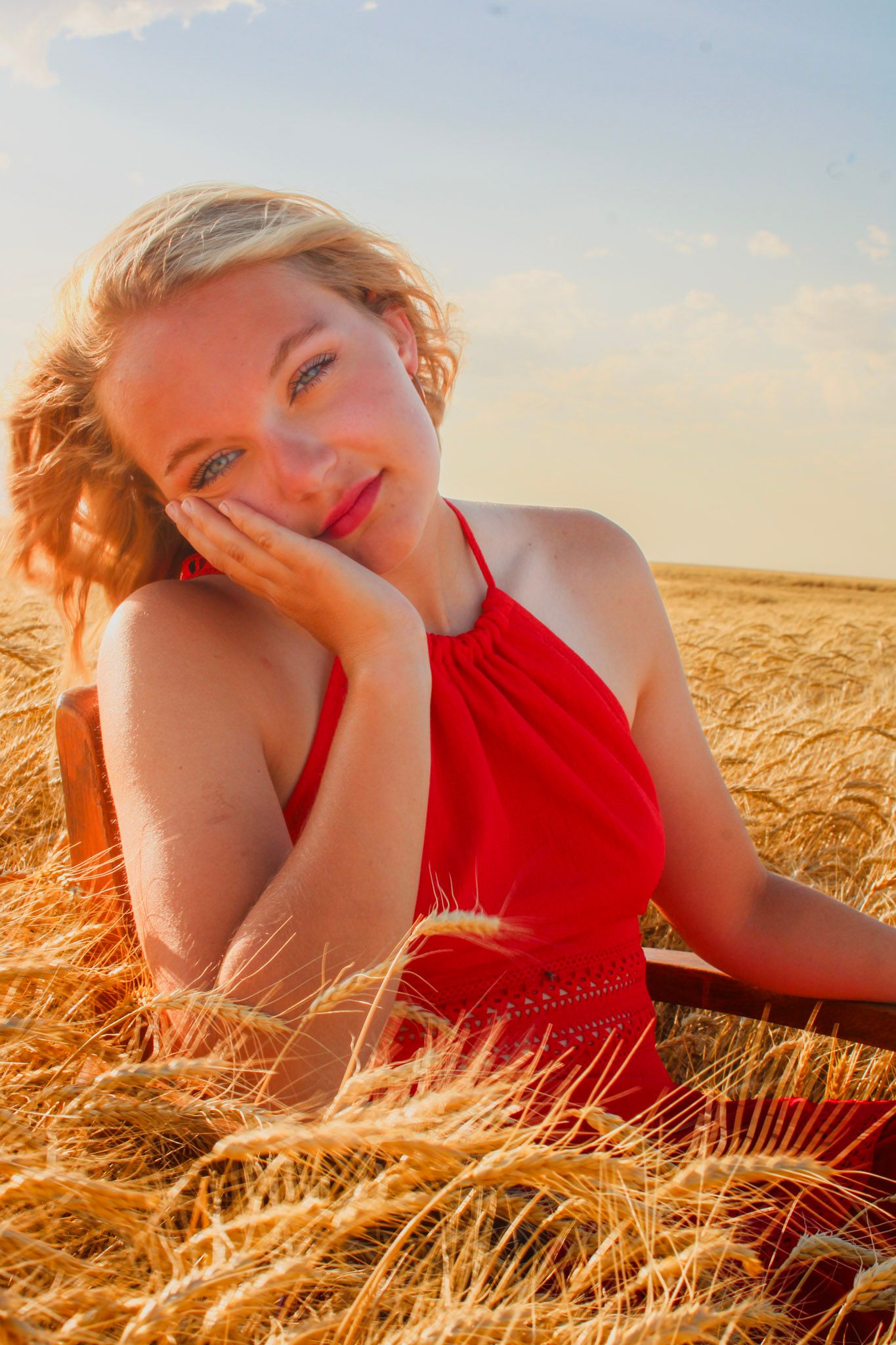 A person in a red dress poses in a golden wheat field at sunset.