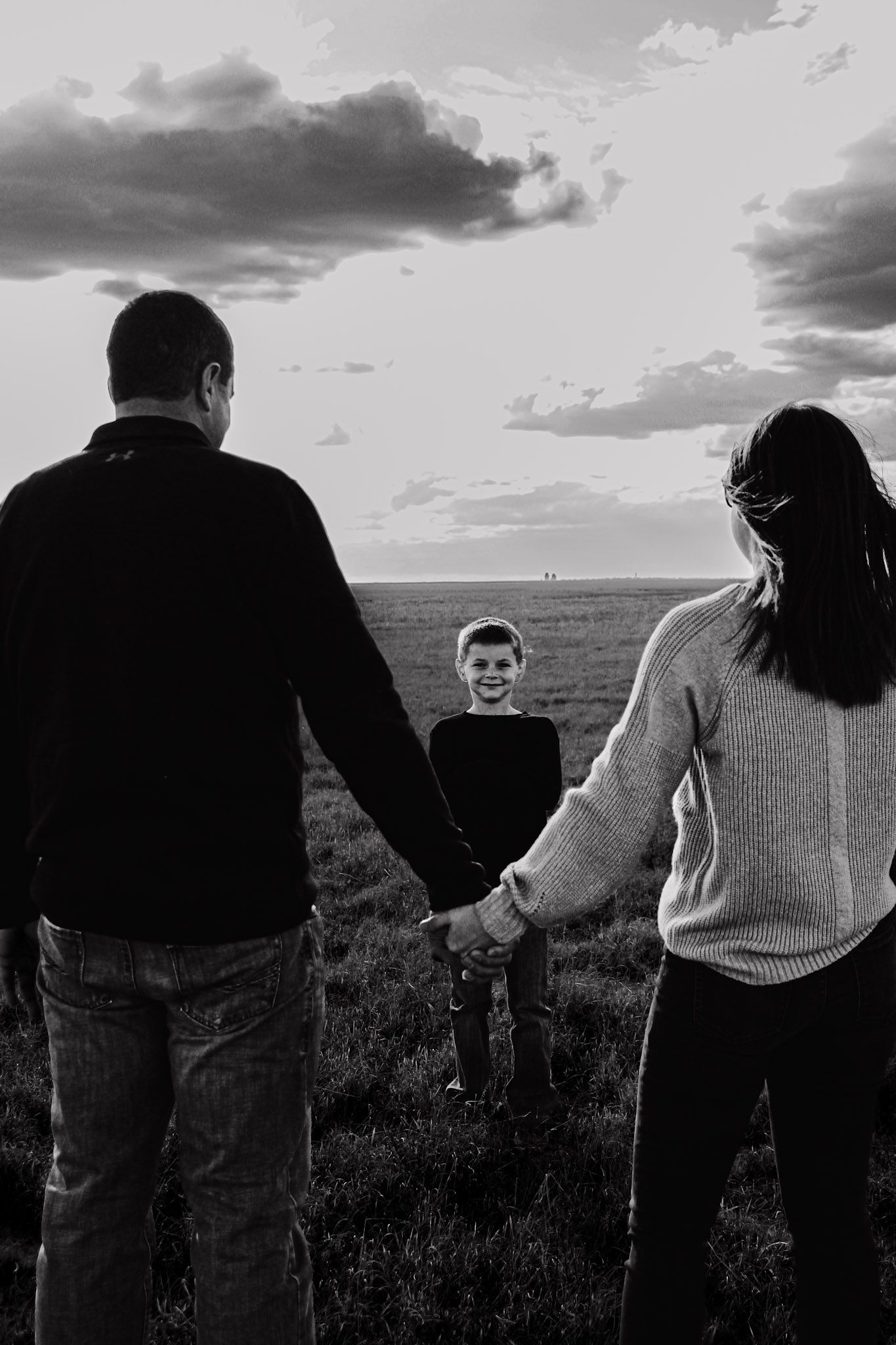 A family stands together silhouetted against a dramatic sunset sky in an open field.