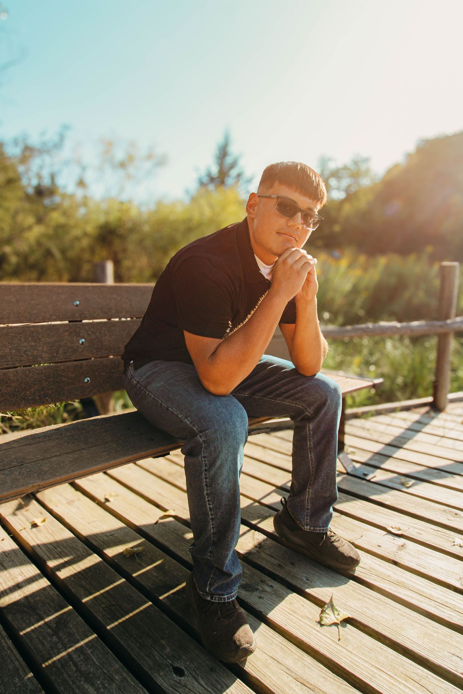 Person sitting on wooden deck in sunlight casting dramatic shadows on planks during golden hour.