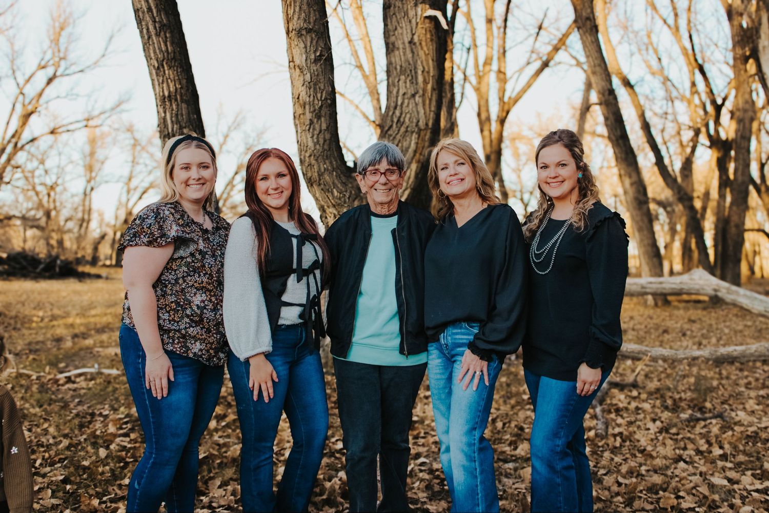Group of five people standing close together posing for a casual outdoor portrait among bare trees.
