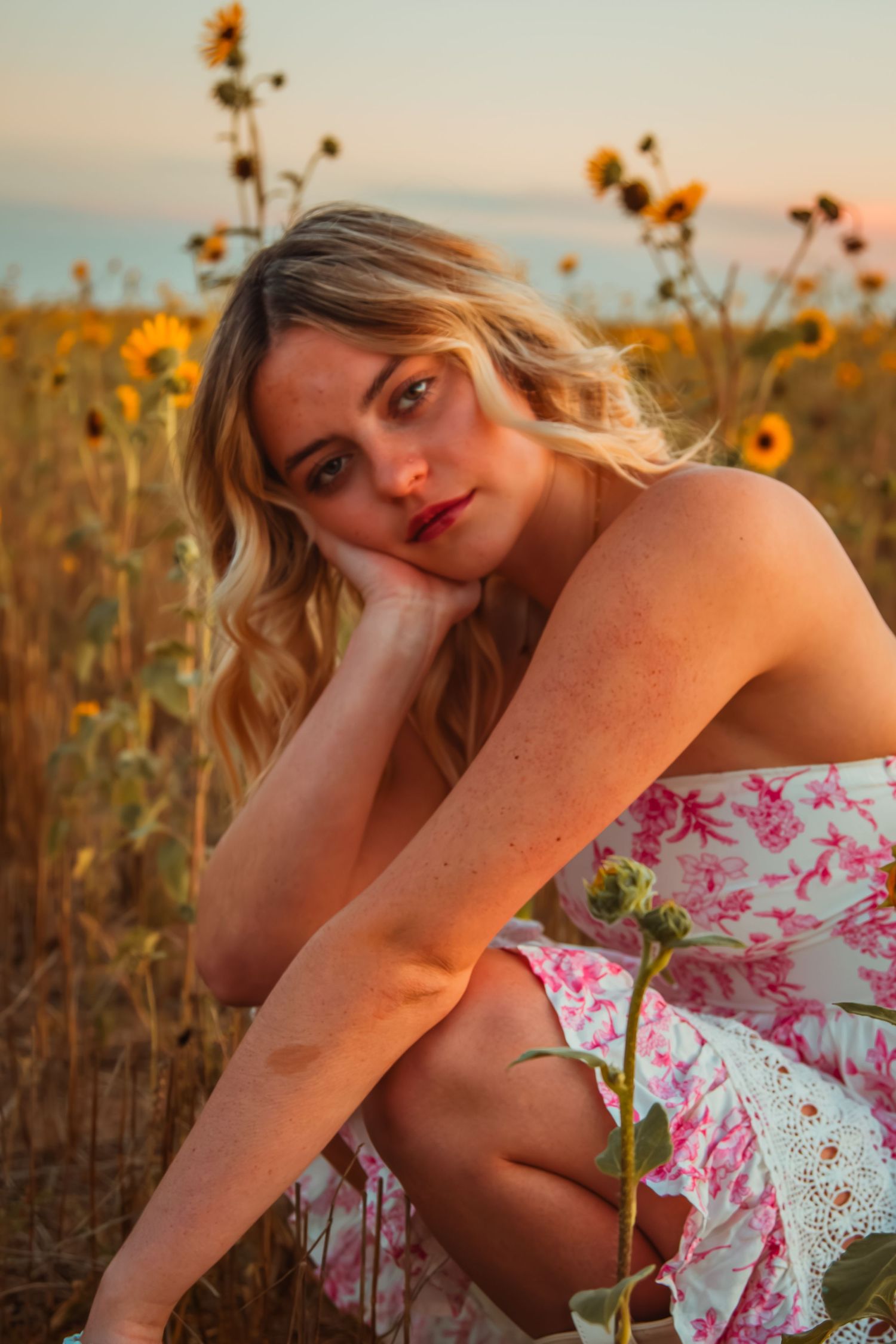 A dreamy sunset portrait in a field of sunflowers with a floral dress and warm golden lighting.