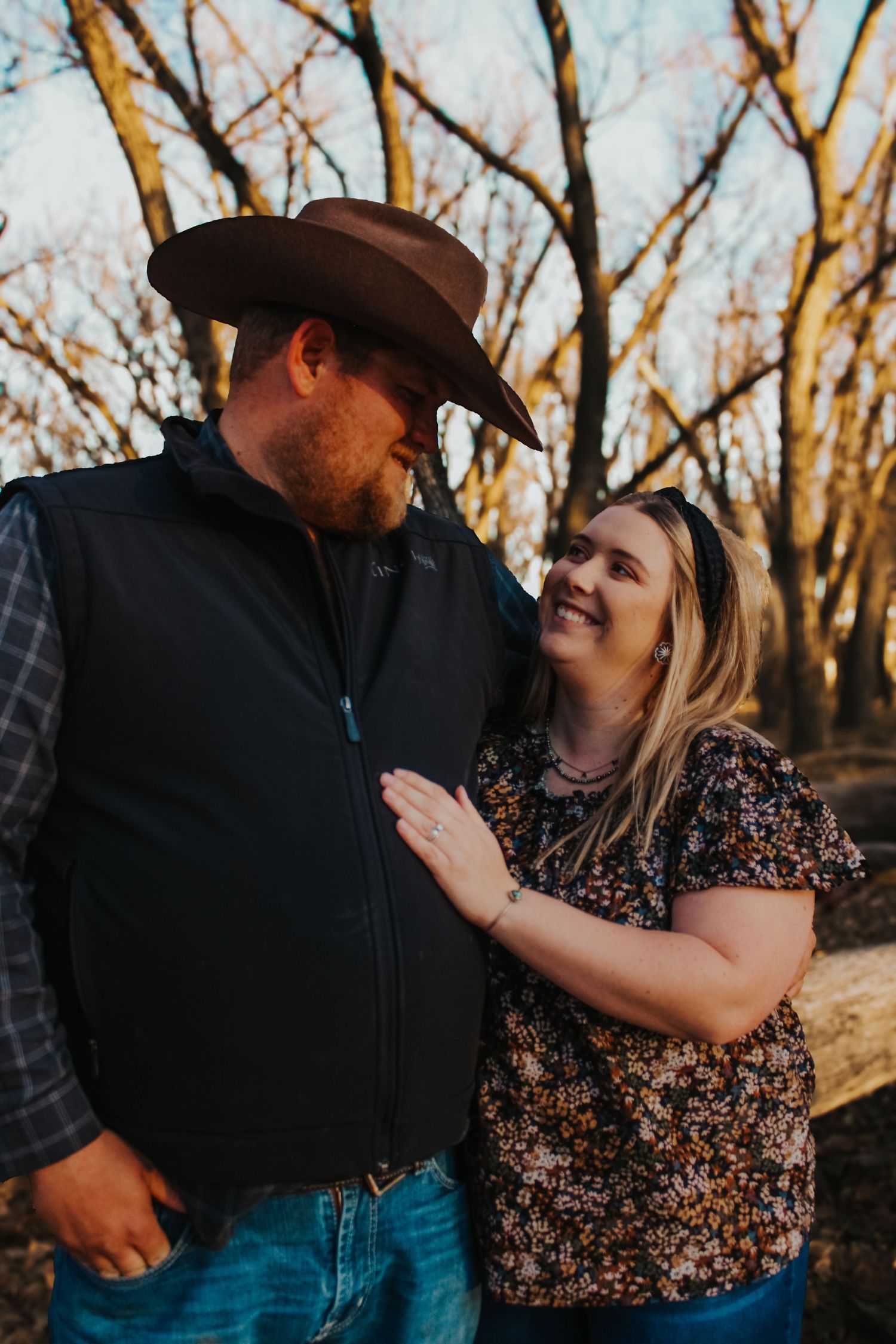 A couple shares a loving glance while posing together in a wooded area during golden hour.