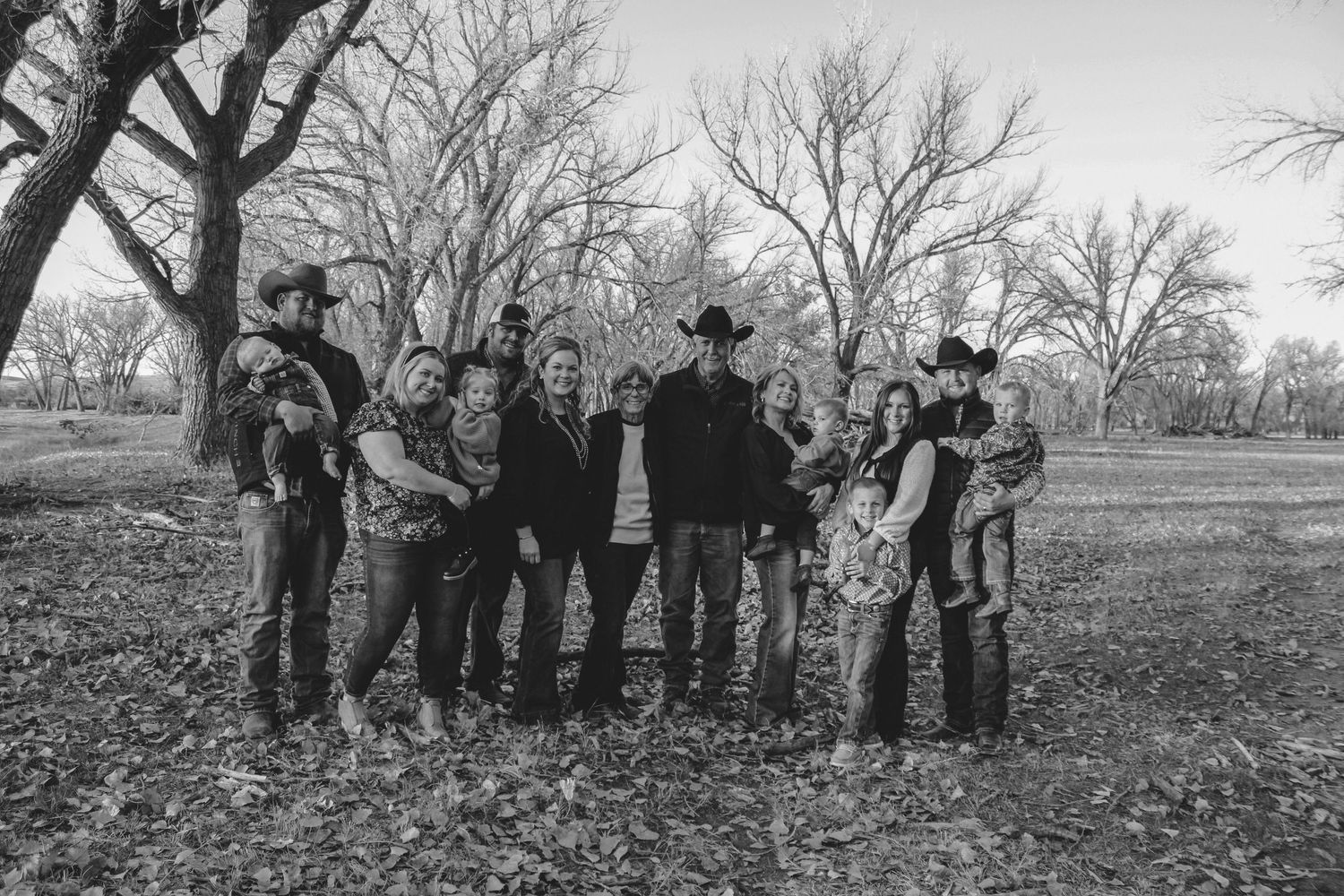 Black and white group portrait of people gathered amongst bare trees in autumn.