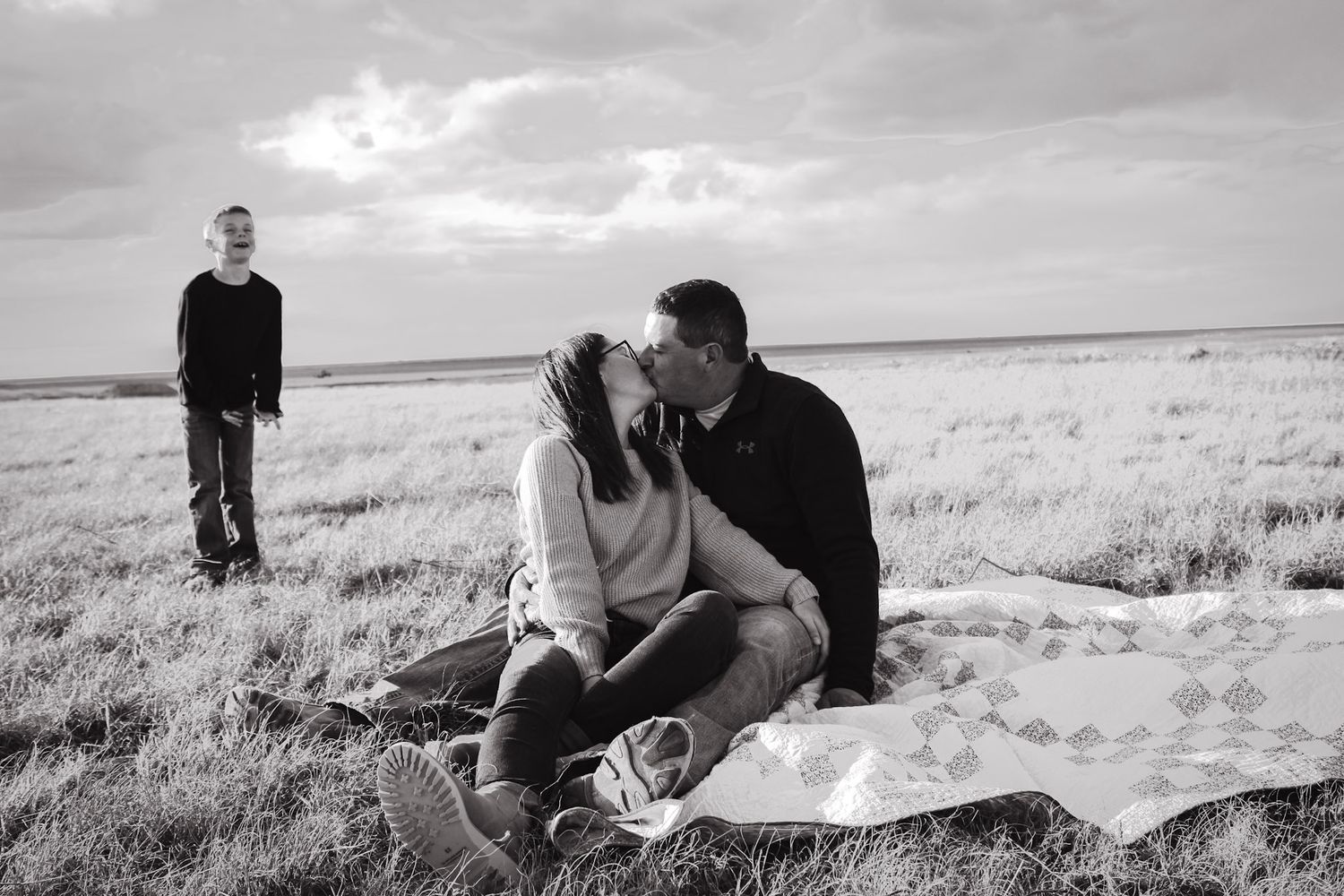 Three people pose in scenic field with dramatic clouds during sunset photoshoot.