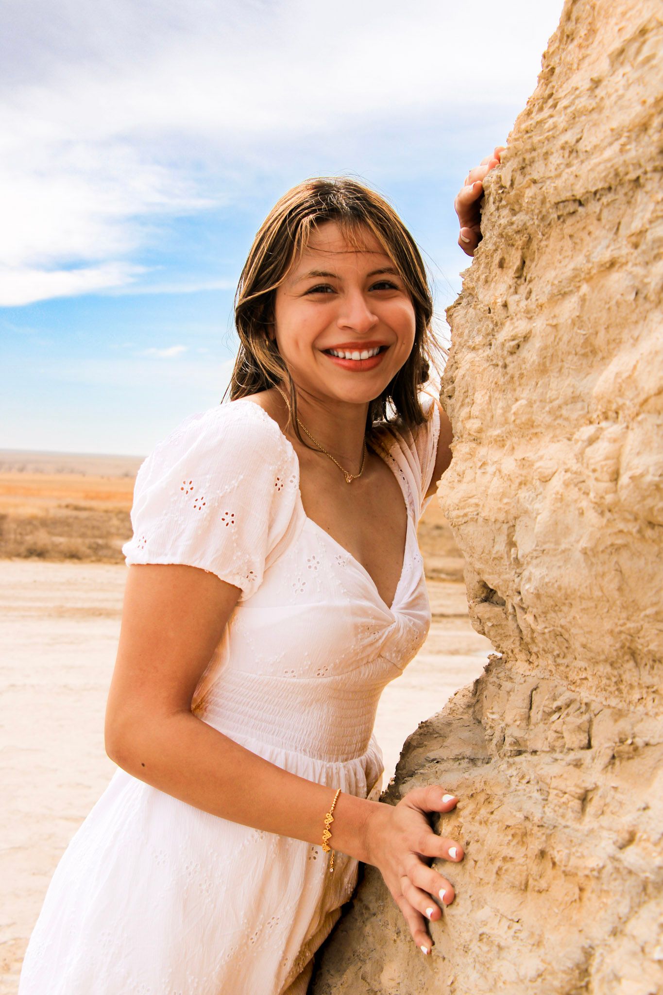 Person in white dress poses playfully against desert rock formations on a sunny day.