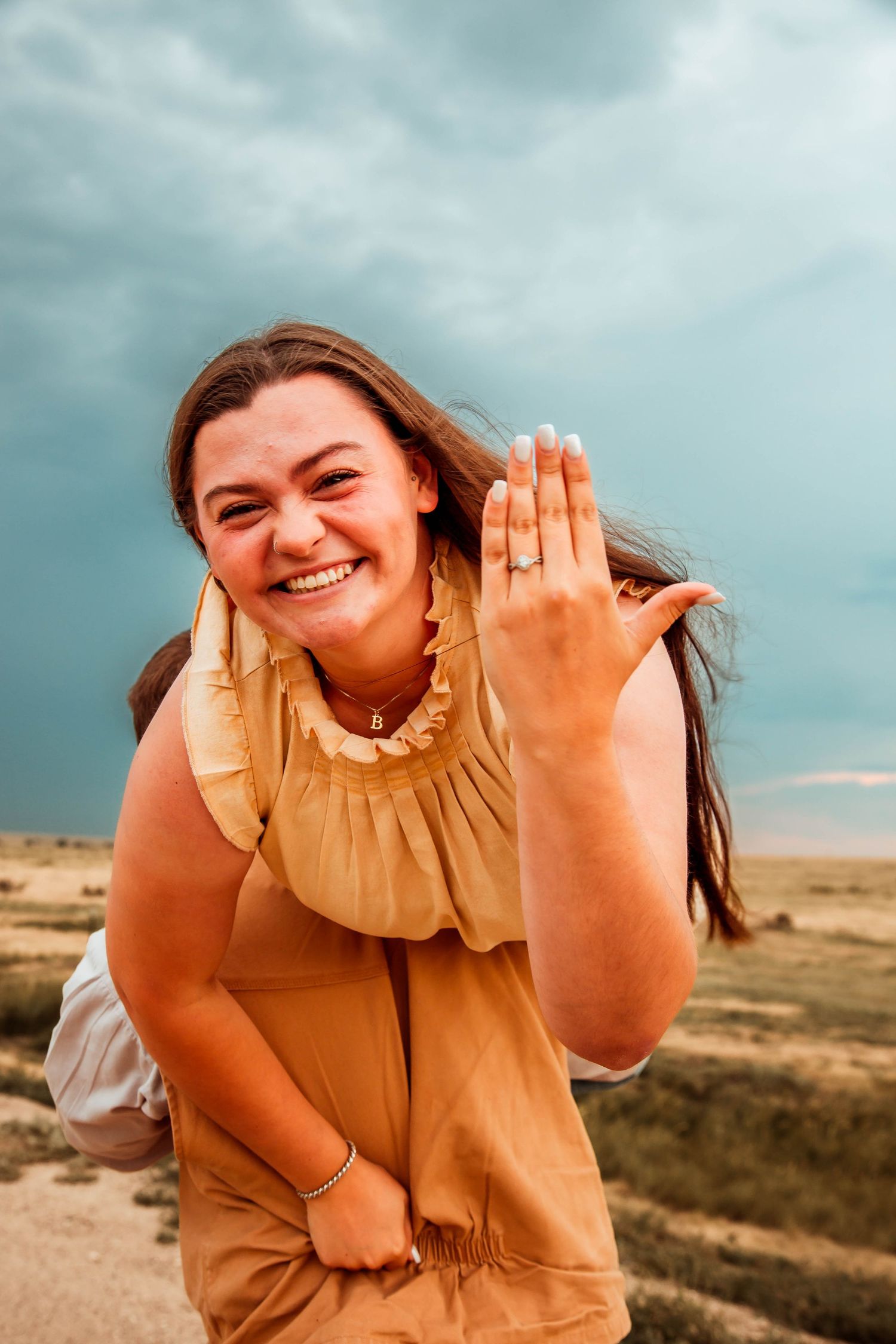 A collage shows someone wearing a tan ruffle dress sitting outdoors in a desert landscape making joyful expressions.