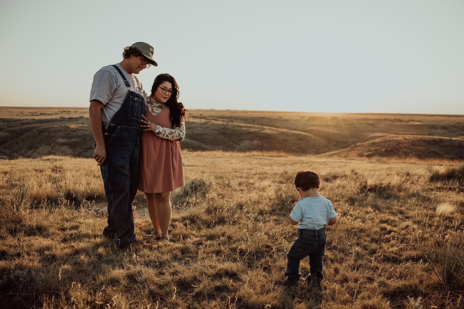 A family shares a tender moment in an open field during golden hour.