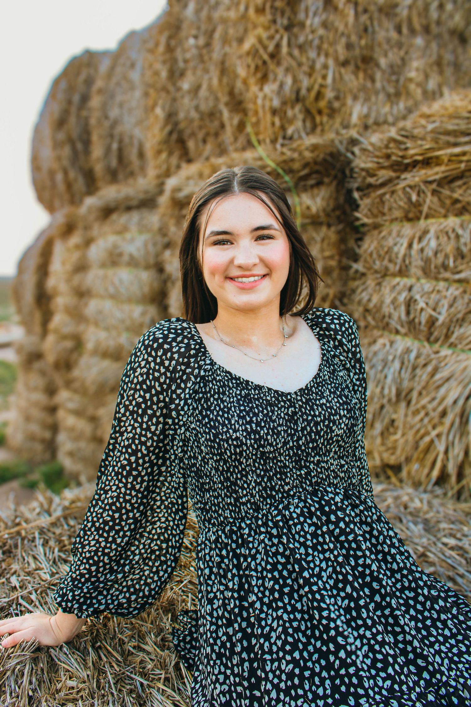 A polka dot dress worn in a rustic outdoor setting with hay bales creating a cozy autumn portrait atmosphere.