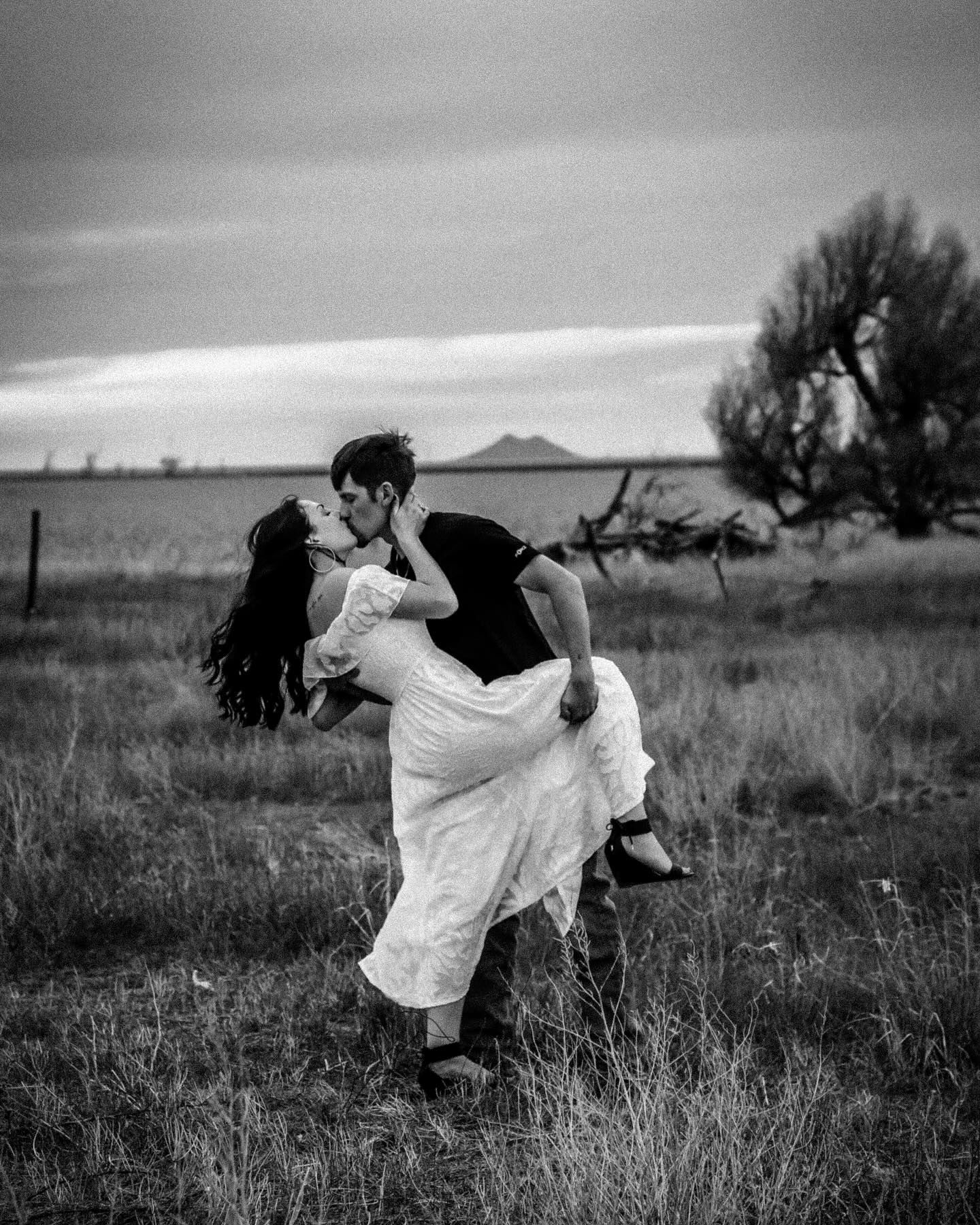 Romantic black and white photograph of a couple dancing in a field with mountains in the background.
