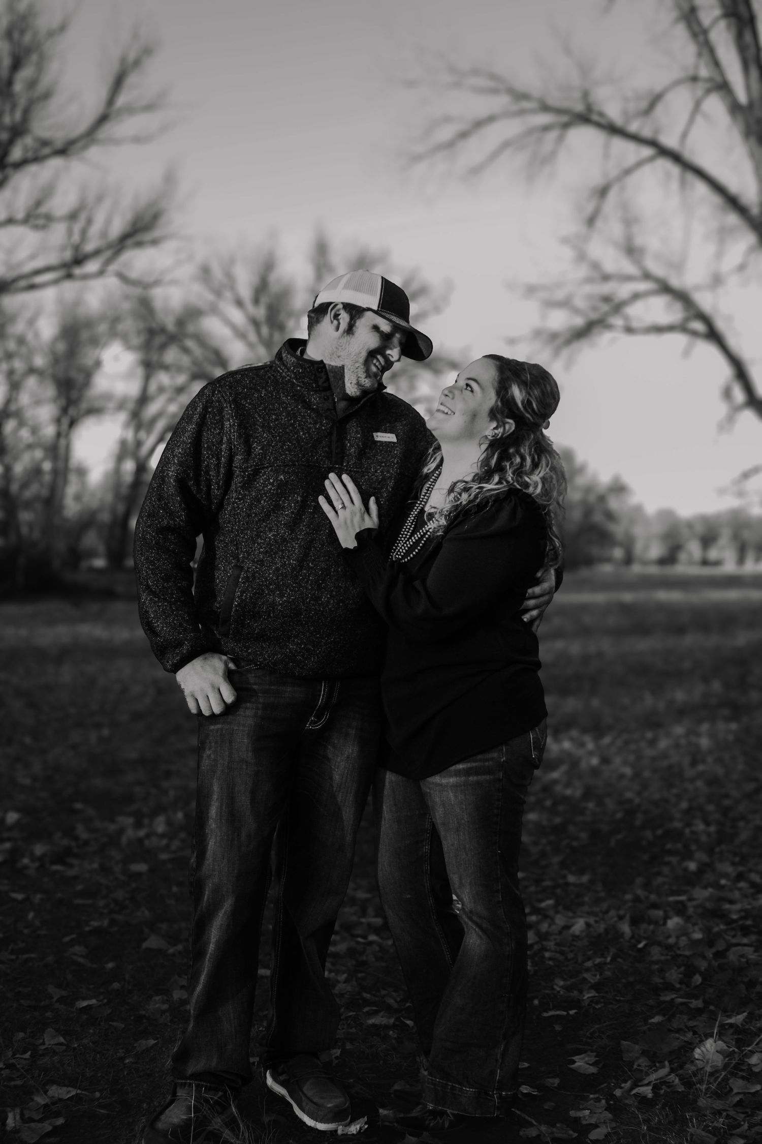 Black and white portrait of a couple sharing a laugh in a wooded setting.