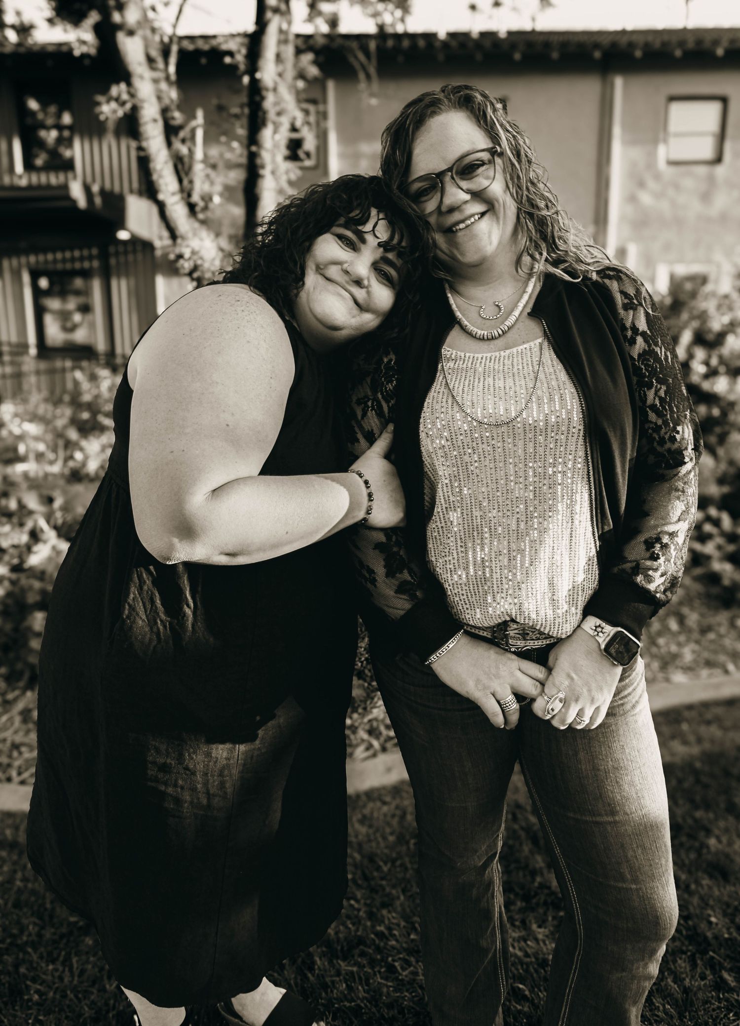 Two friends sharing a warm embrace and laughing together in a black and white portrait.