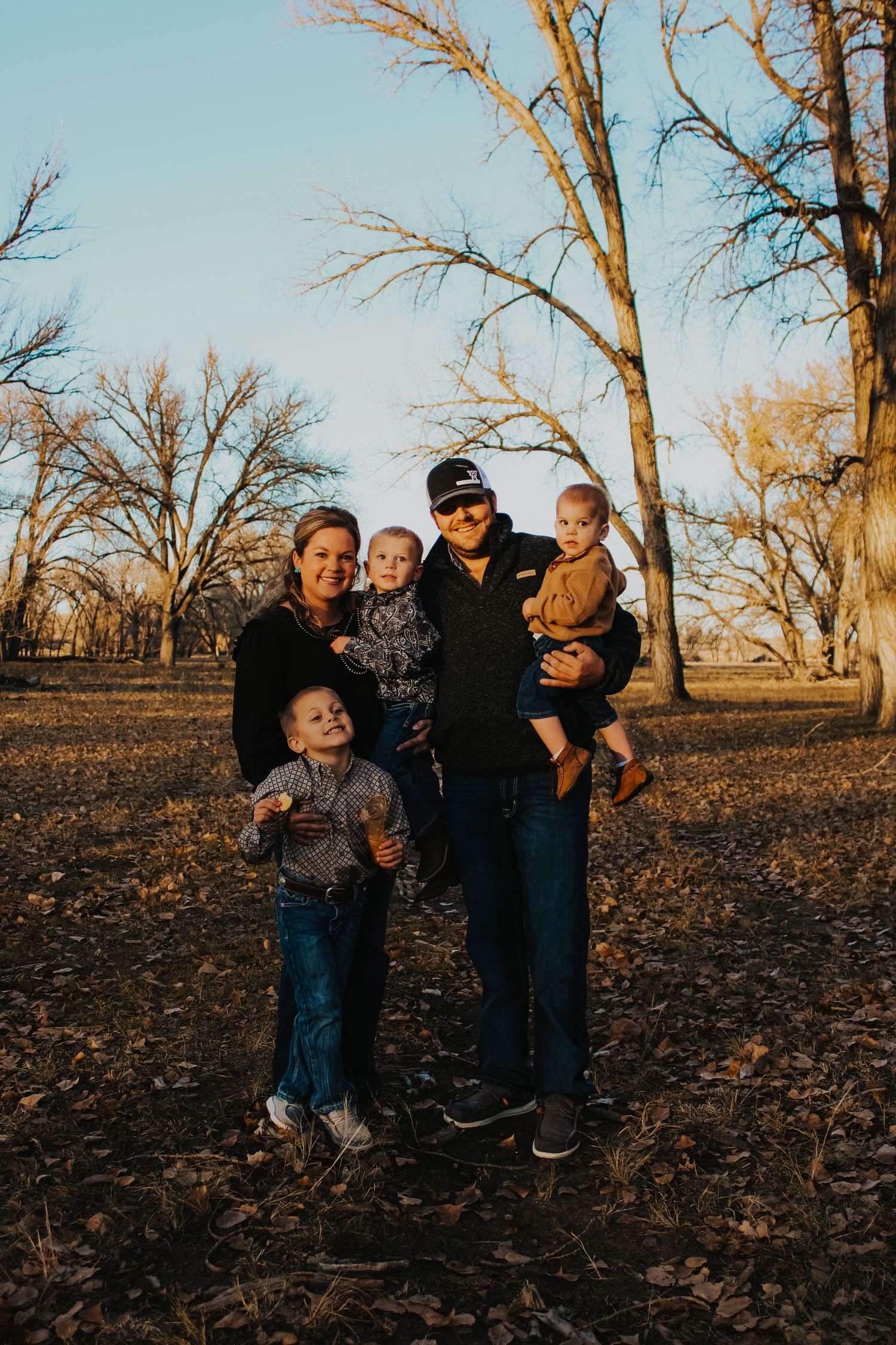 Family gathering under bare trees during golden hour in a park.