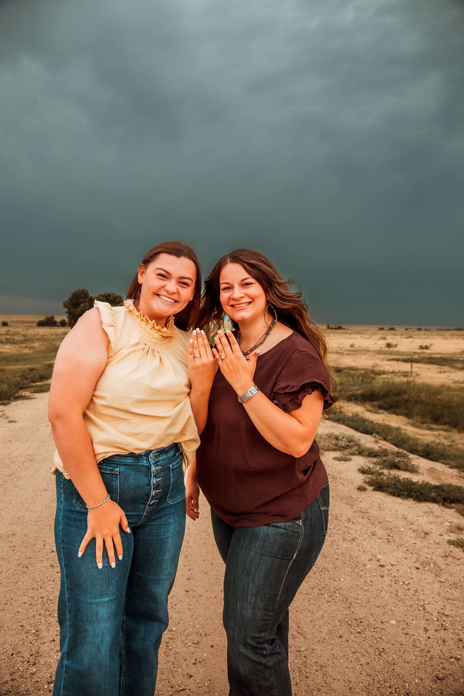 Joyful couple embracing on a dirt path against stormy dramatic clouds during a countryside photoshoot.