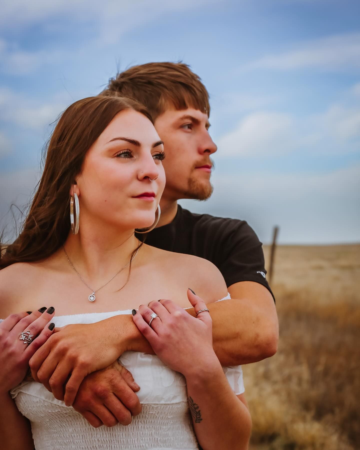 A romantic engagement photo shows a couple embracing in a golden field at sunset.