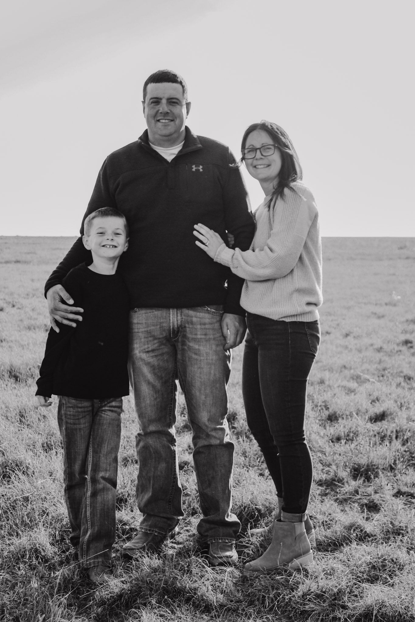A casual outdoor family portrait taken in a grassy field on an overcast day.
