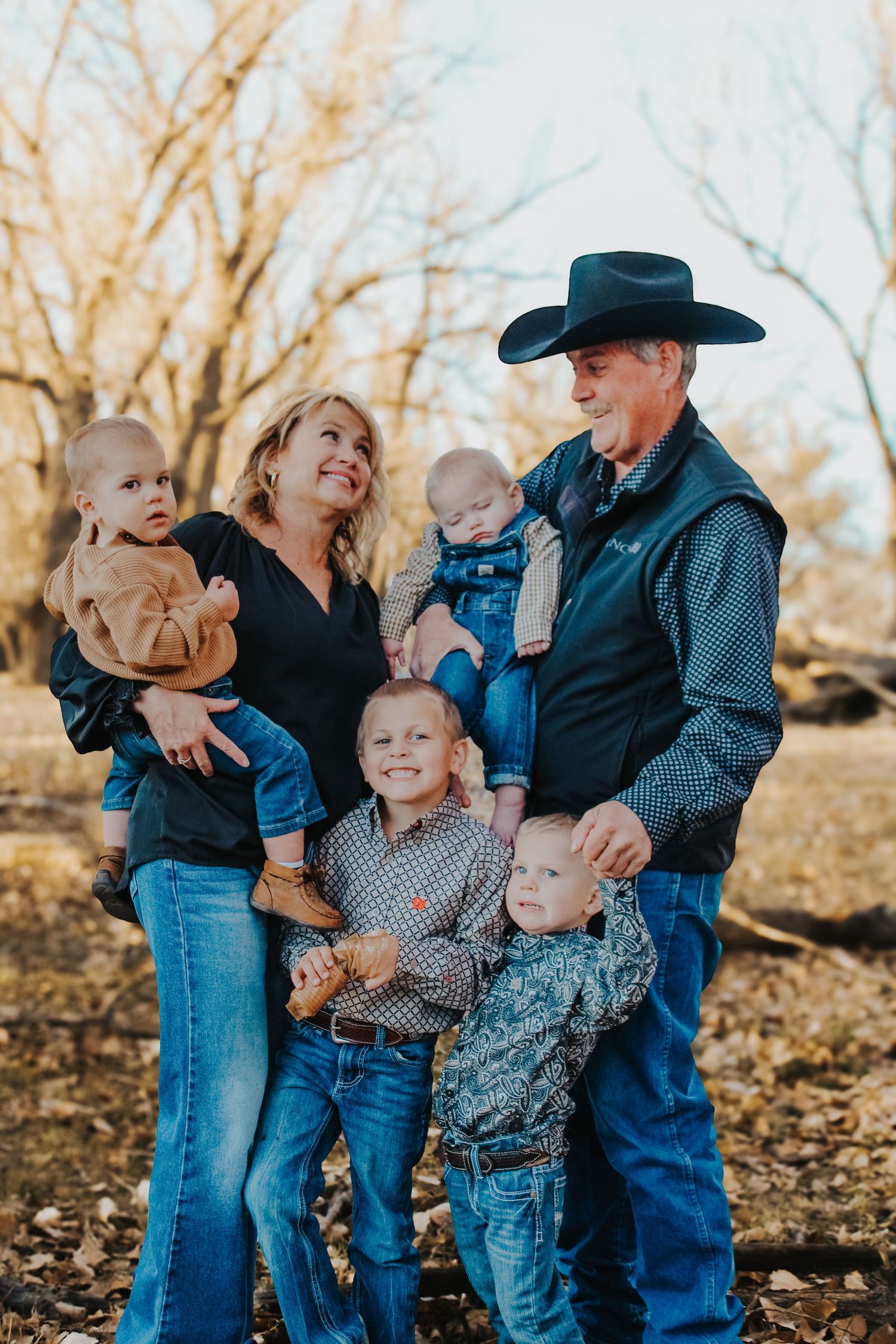 Family portrait in western wear standing among autumn trees.