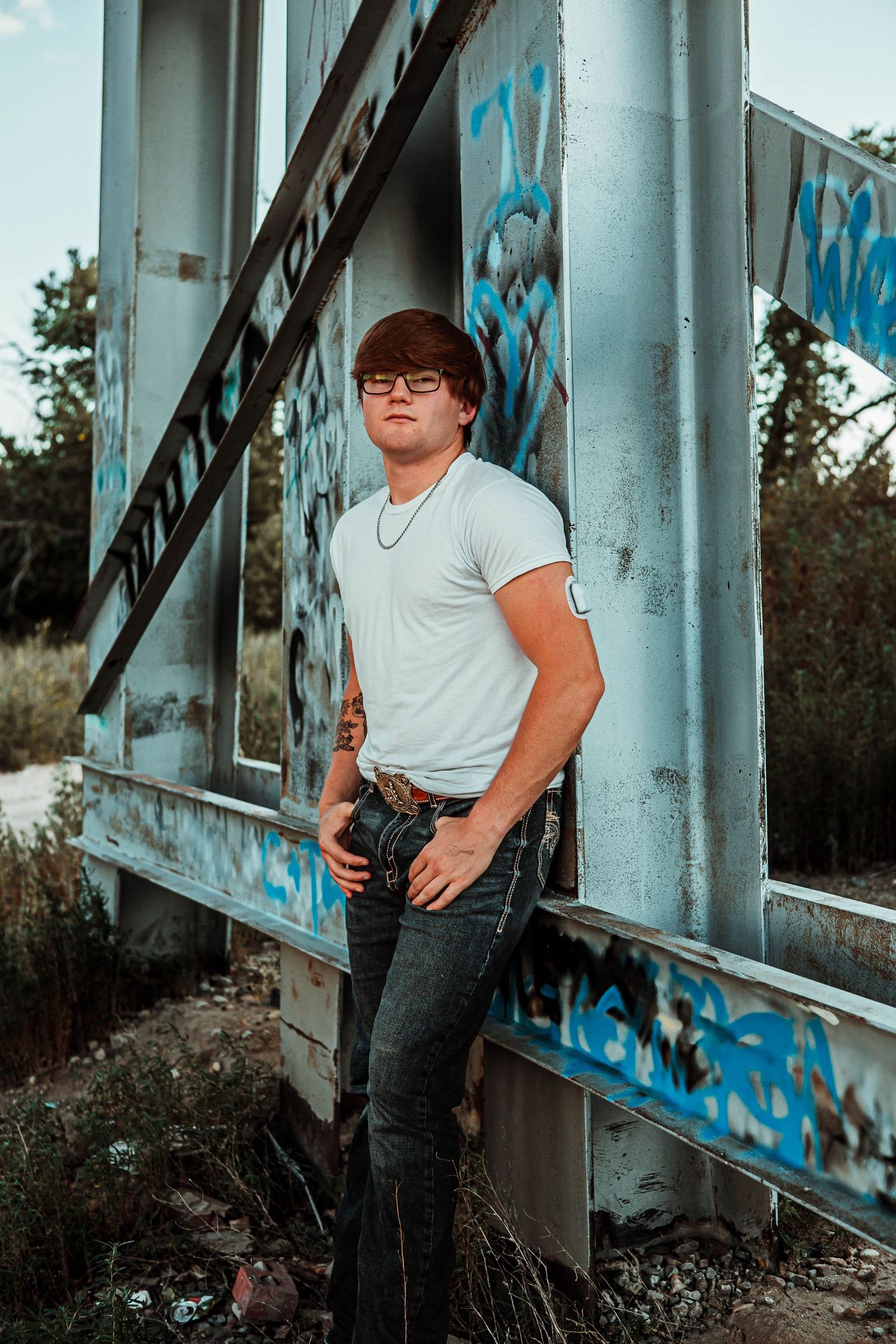 A person in a white t-shirt and jeans leans against a concrete wall with blue graffiti in a series of artistic poses.