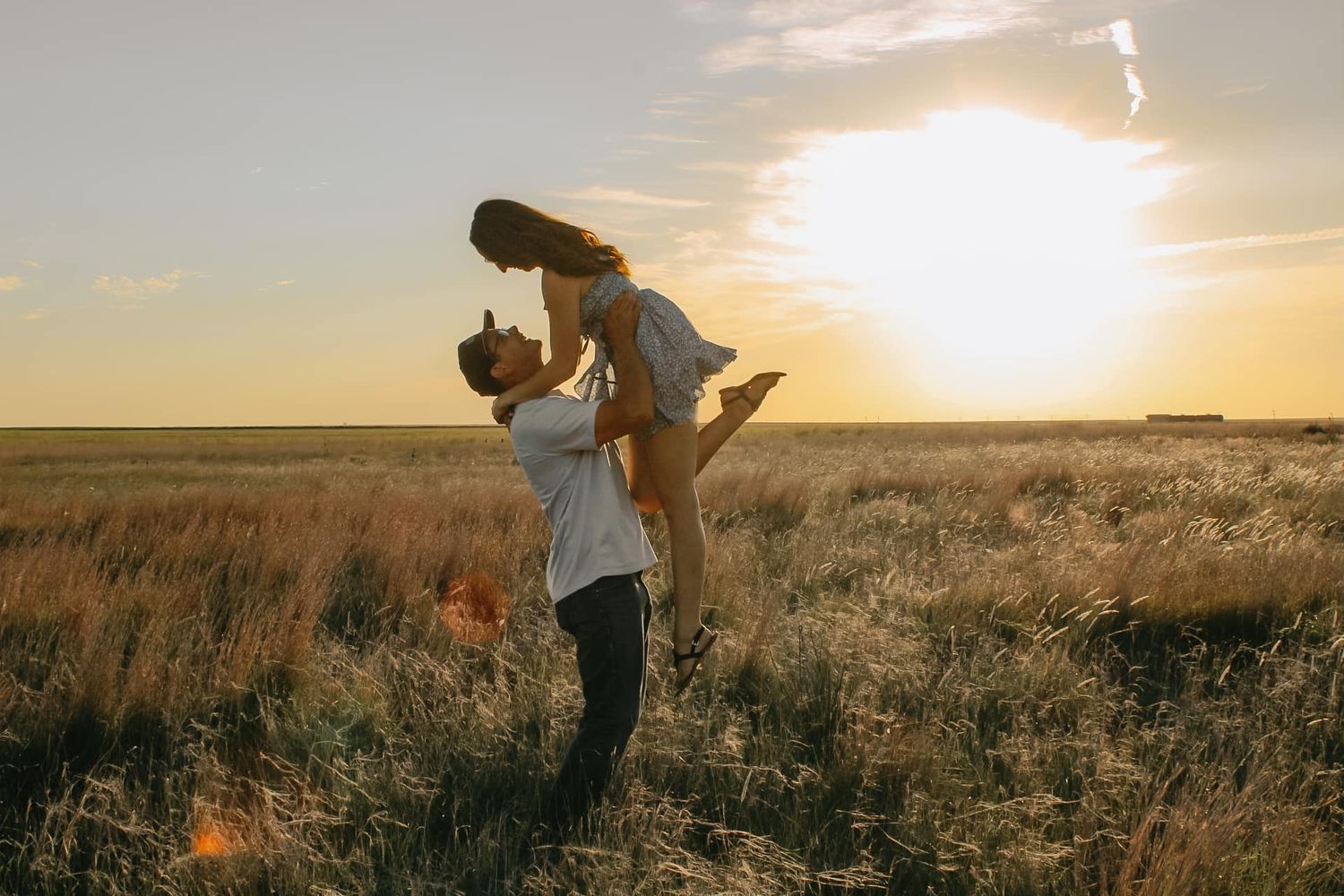 A joyful couple plays in a field during sunset as one lifts the other.
