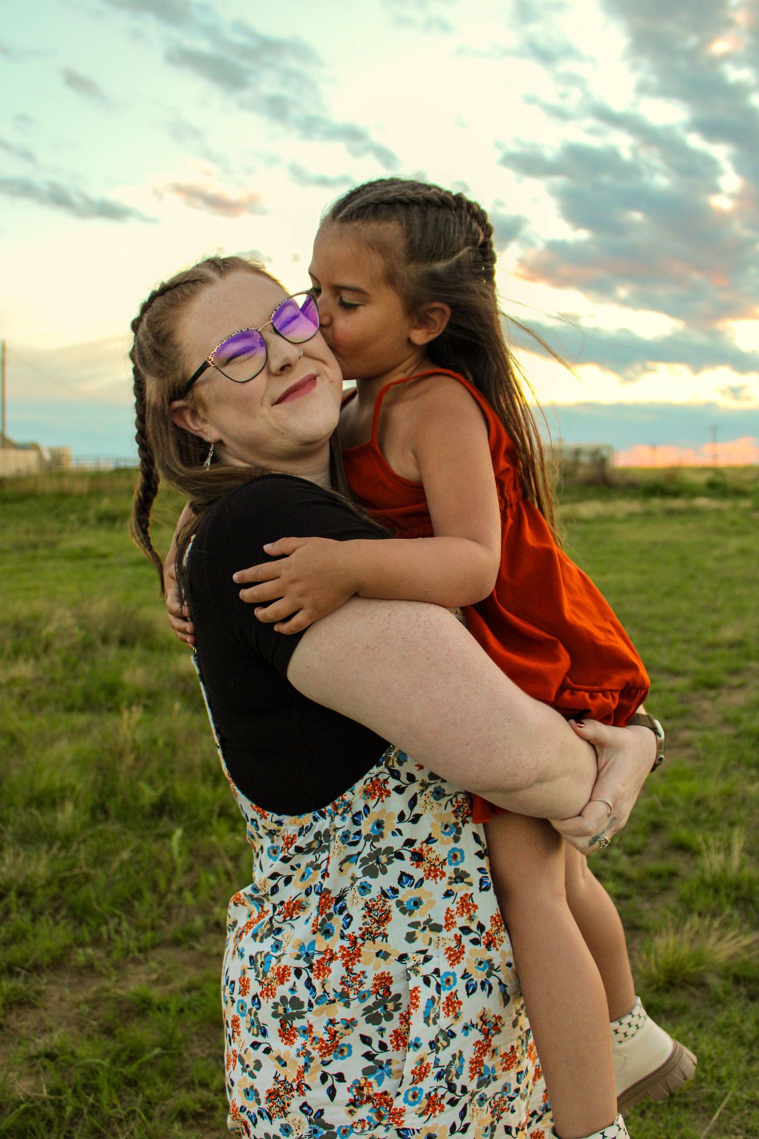 An affectionate moment captured outdoors at sunset in a grassy field.