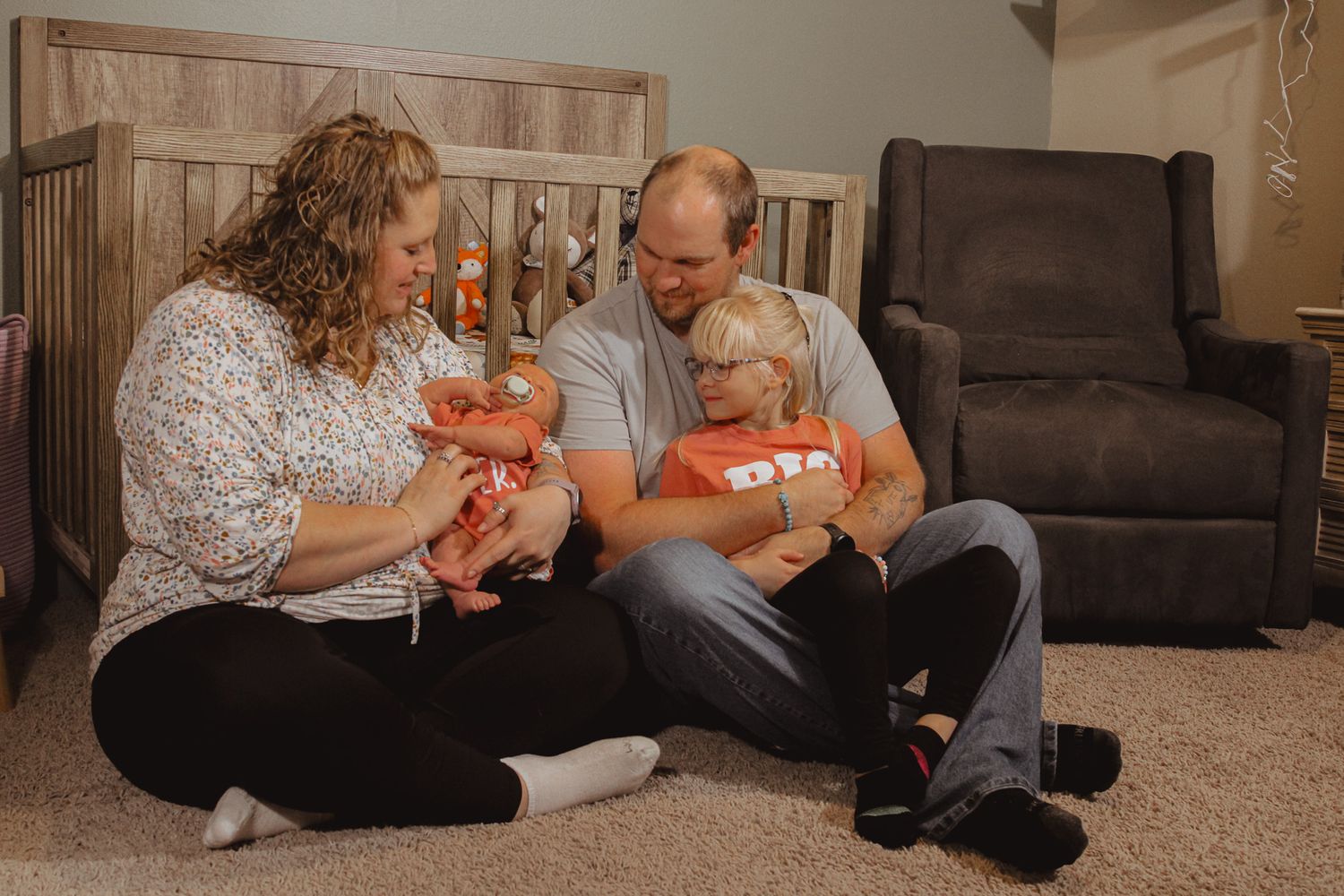 Family sitting on carpet together with infants.