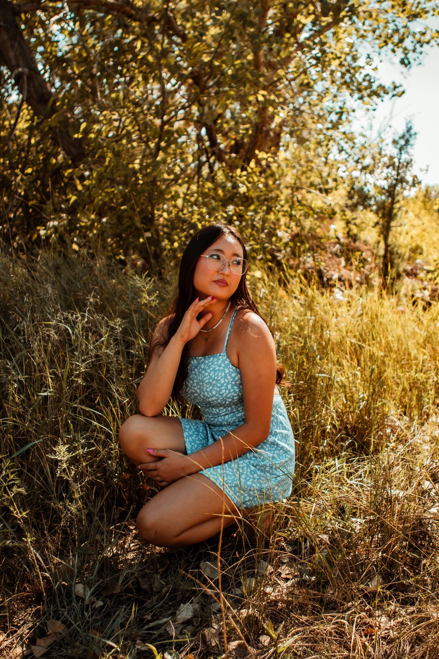 A person in a blue polka dot dress poses thoughtfully in a golden sunlit field during a summer photoshoot.
