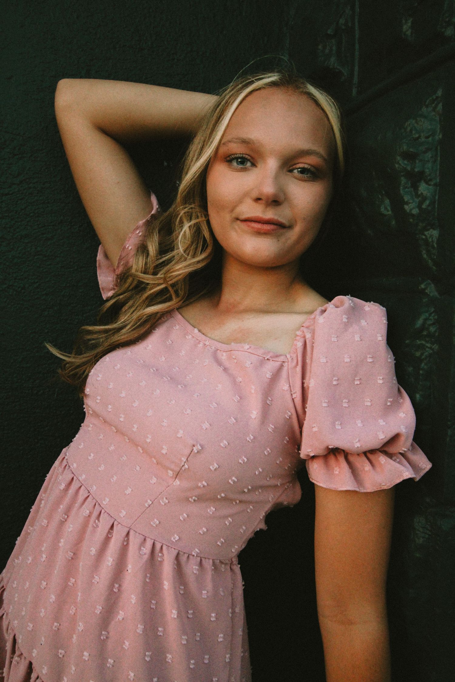 A person in a pink dotted dress with puff sleeves poses against a dark background.