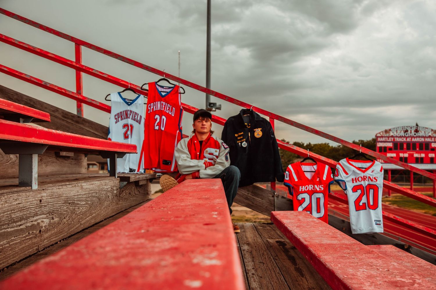 Sports jerseys displayed on red stadium bleachers under dramatic cloudy sky.