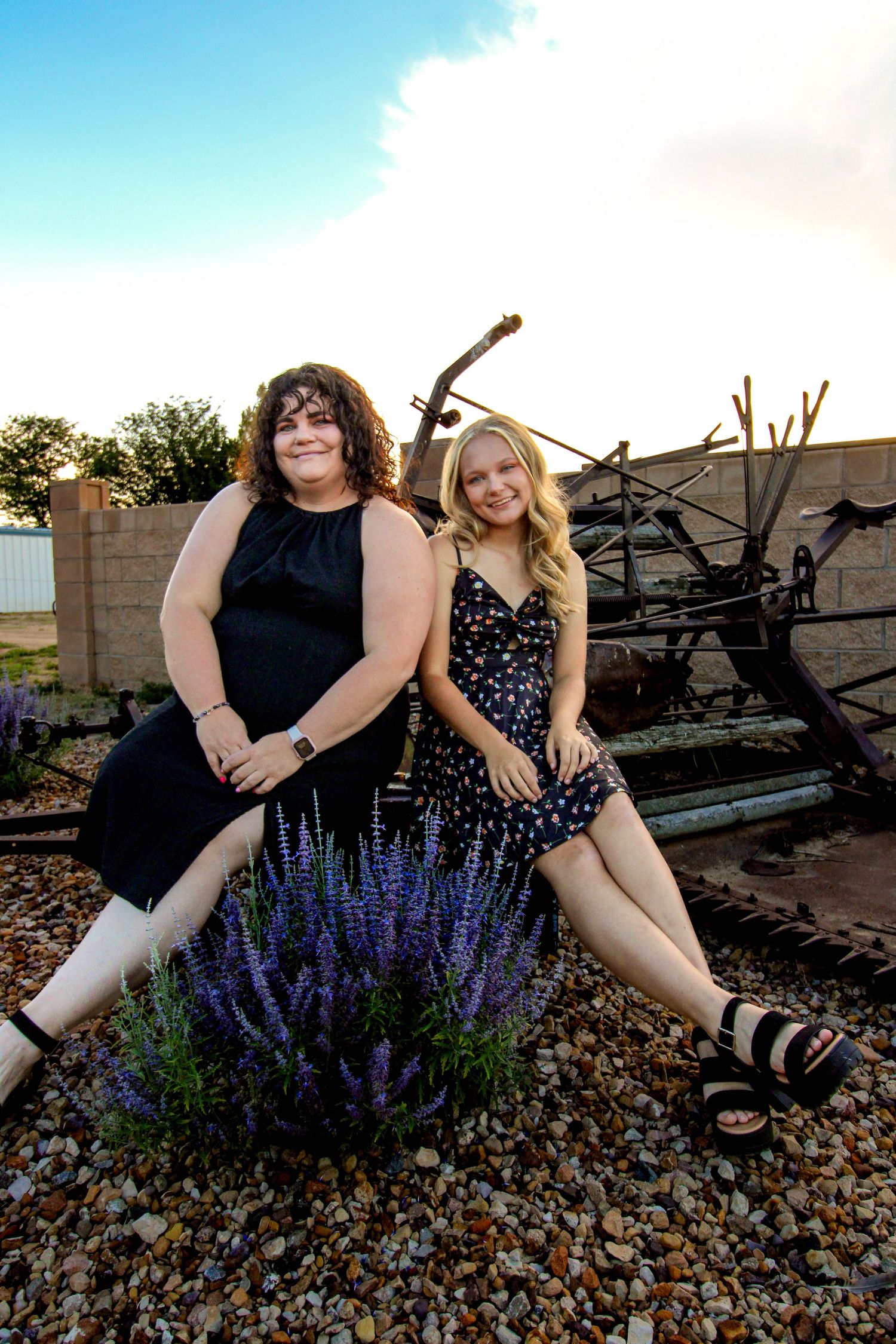 Two women sit beside purple flowers in a desert garden with rustic decor.