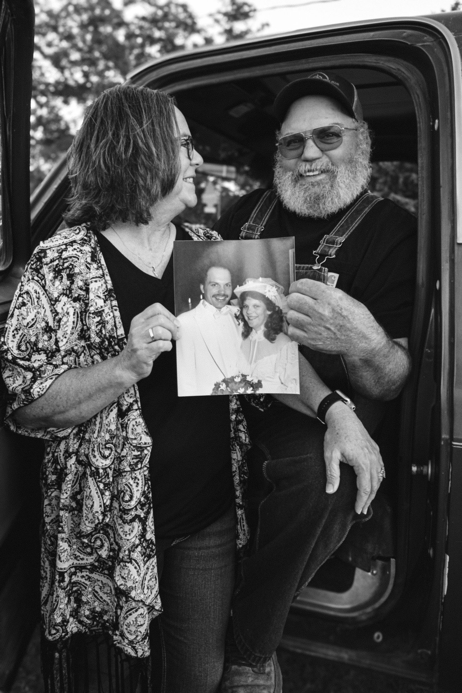 Two people sitting in a vehicle sharing an old photograph together in black and white.