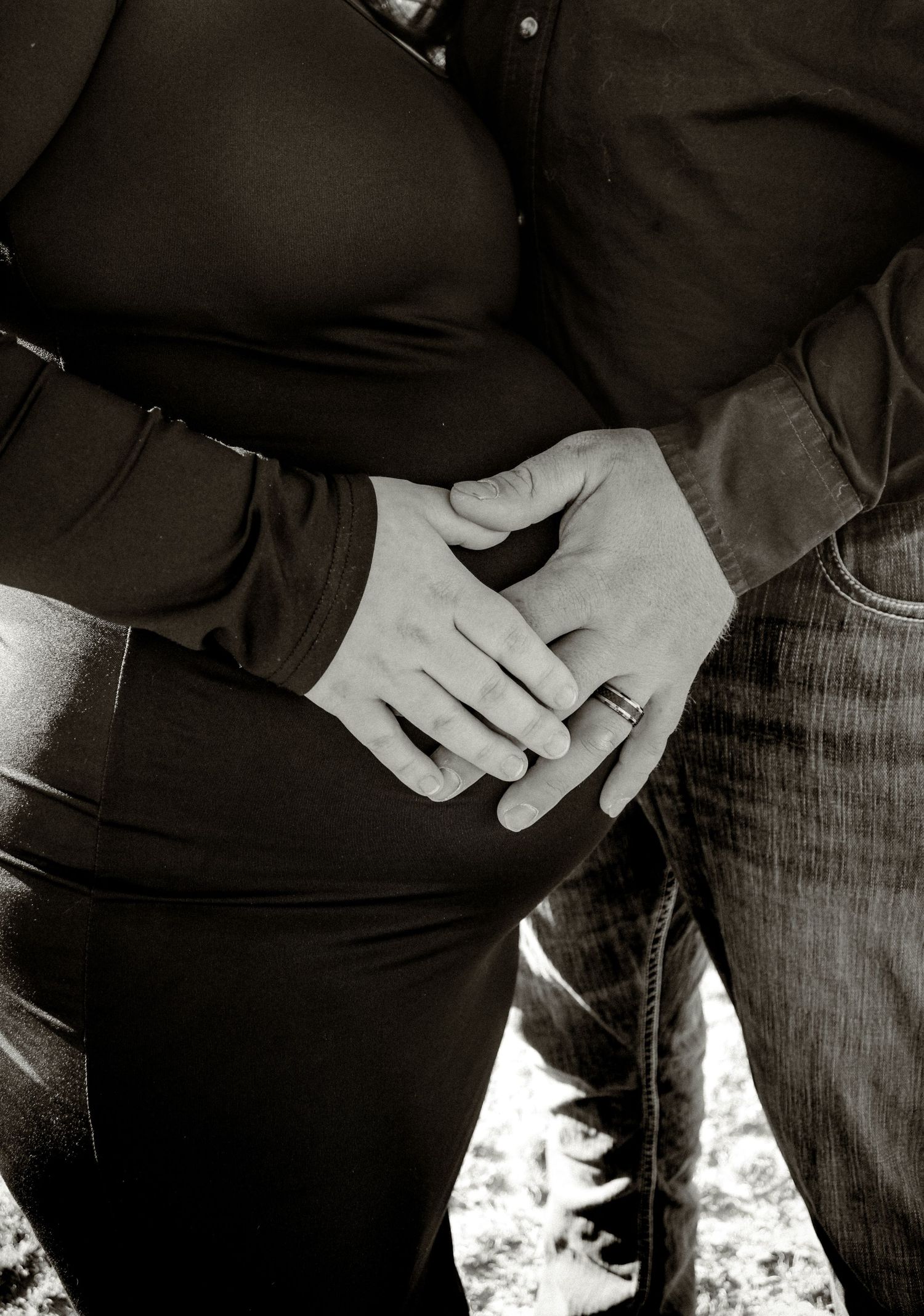 Black and white closeup photo of two hands wearing rings with one resting on a woman's pregnant belly.