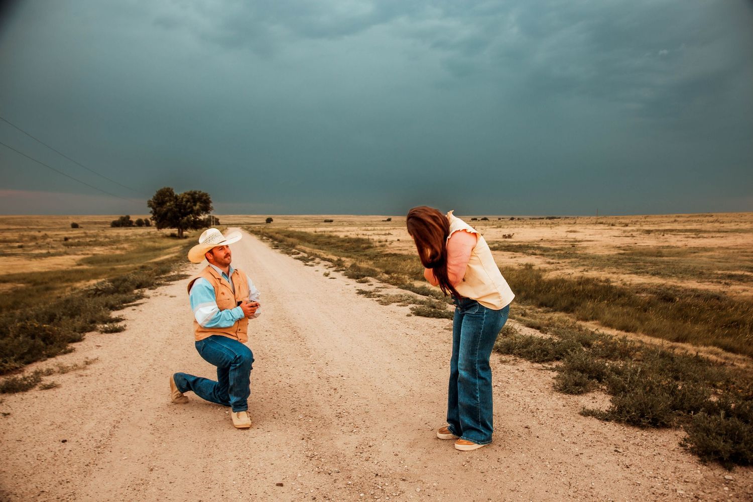A dramatic proposal moment on a dusty country road under stormy skies with dark clouds looming overhead.