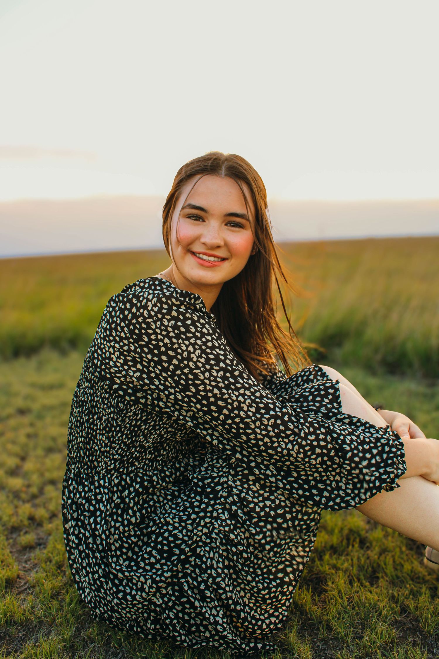 Person in a polka dot dress poses playfully in a golden field during sunset.