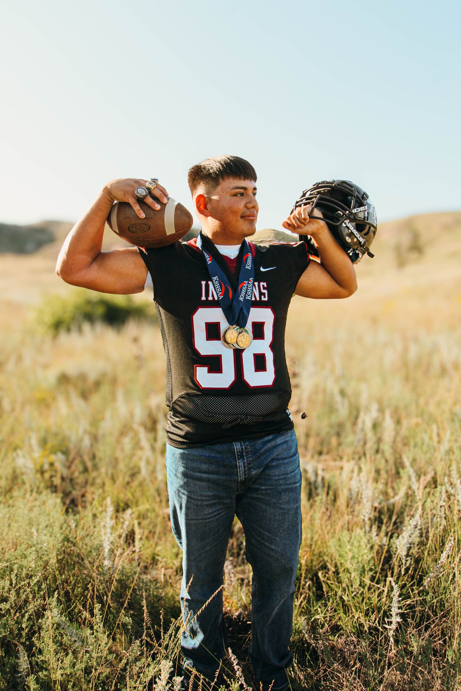 Football player poses in a field wearing jersey number 98 against a golden sunset backdrop.