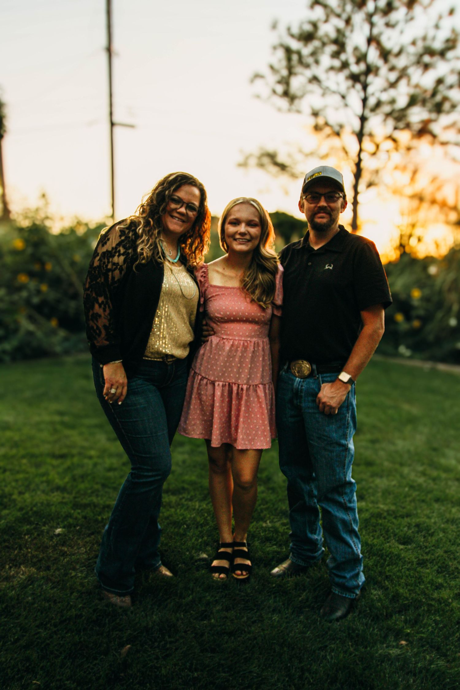 Three people pose together at sunset in a backyard garden setting.