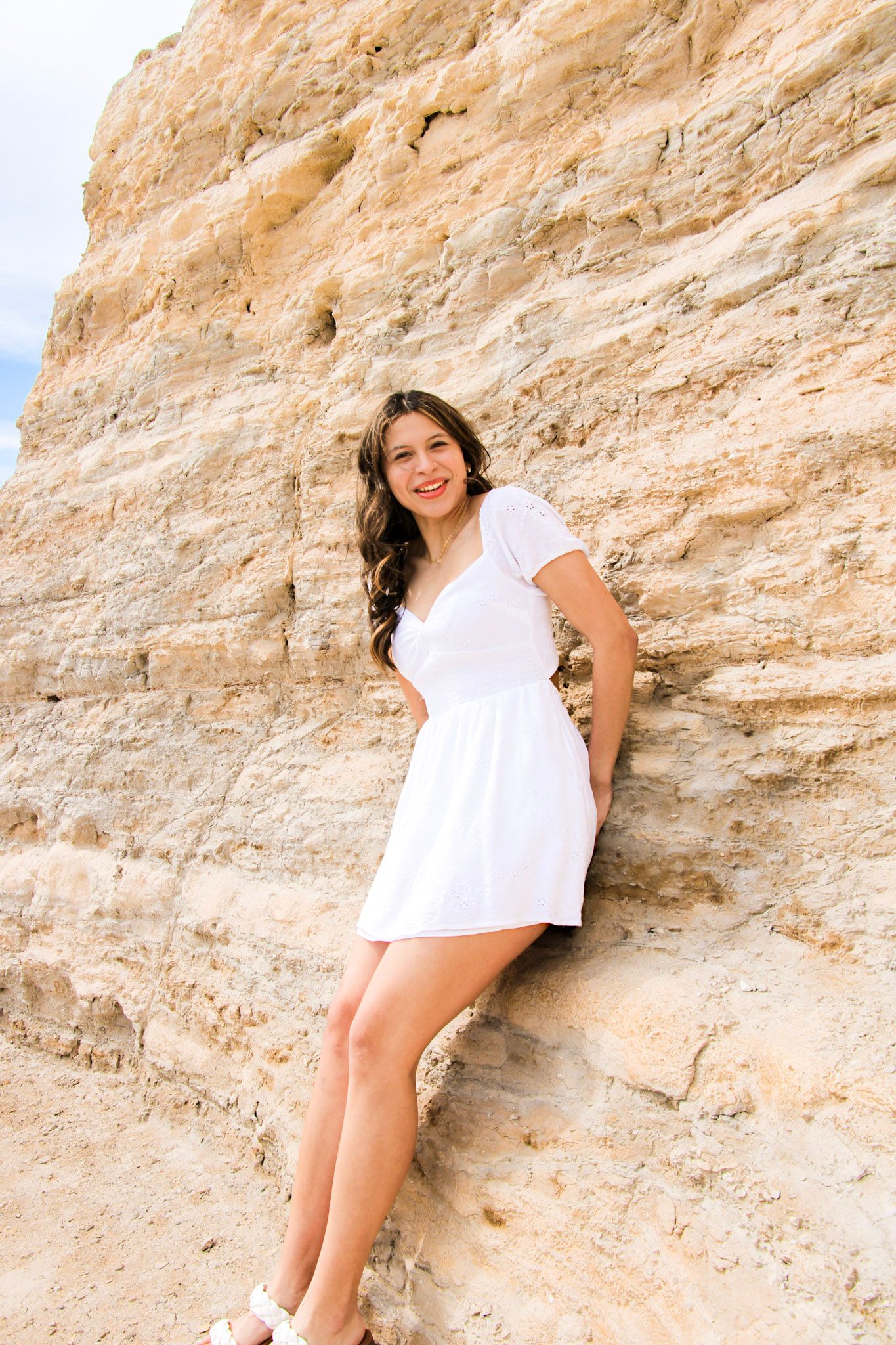 Person in white dress poses against a textured limestone cliff wall in a series of artistic outdoor shots.