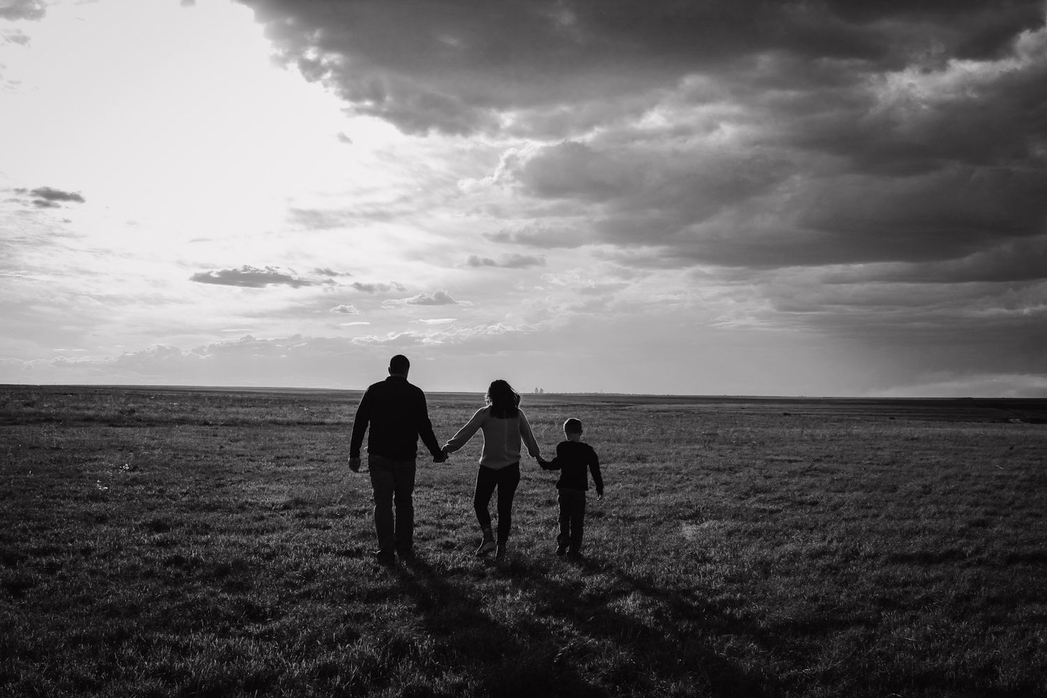 Silhouette of family walking hand in hand across open field at sunset.